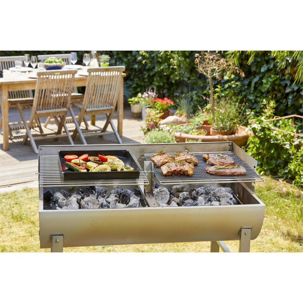 Fleisch und Gemüse werden auf einem Grill im Freien zubereitet, mit einem Tisch im Hintergrund.
