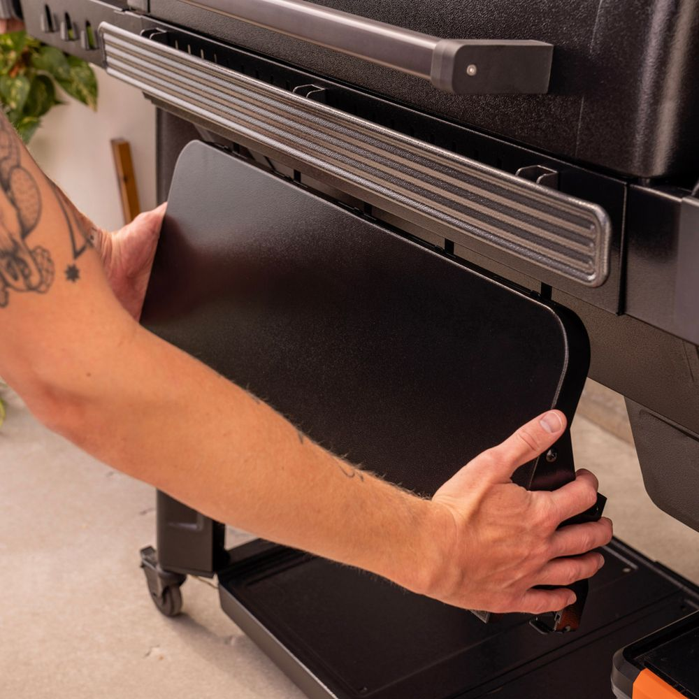 Eine Person montiert eine schwarze Seitenablage an einen Grill.