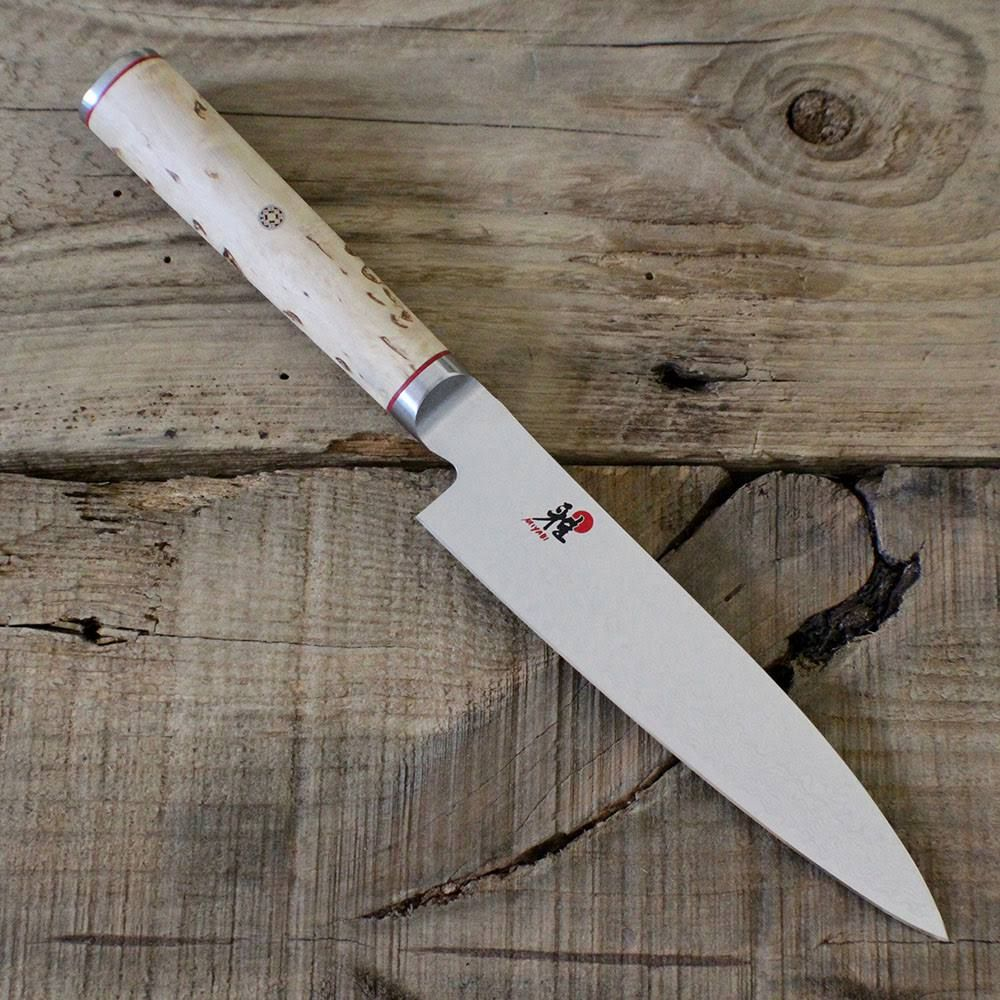 Ein Kochmesser mit hellem Holzgriff liegt auf Holzbrettern.