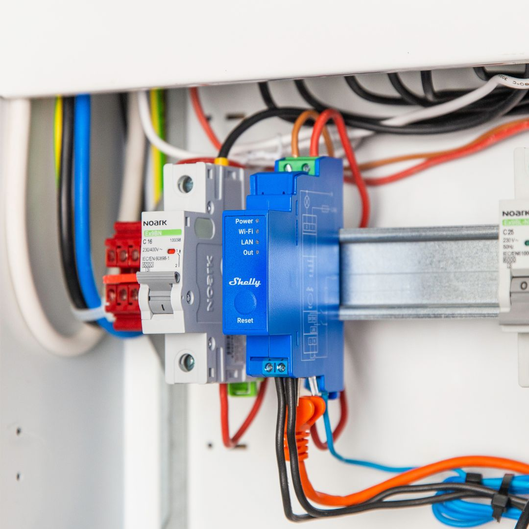 Niebieskie urządzenie Shelly z przewodami i wyłącznikami w panelu elektrycznym.