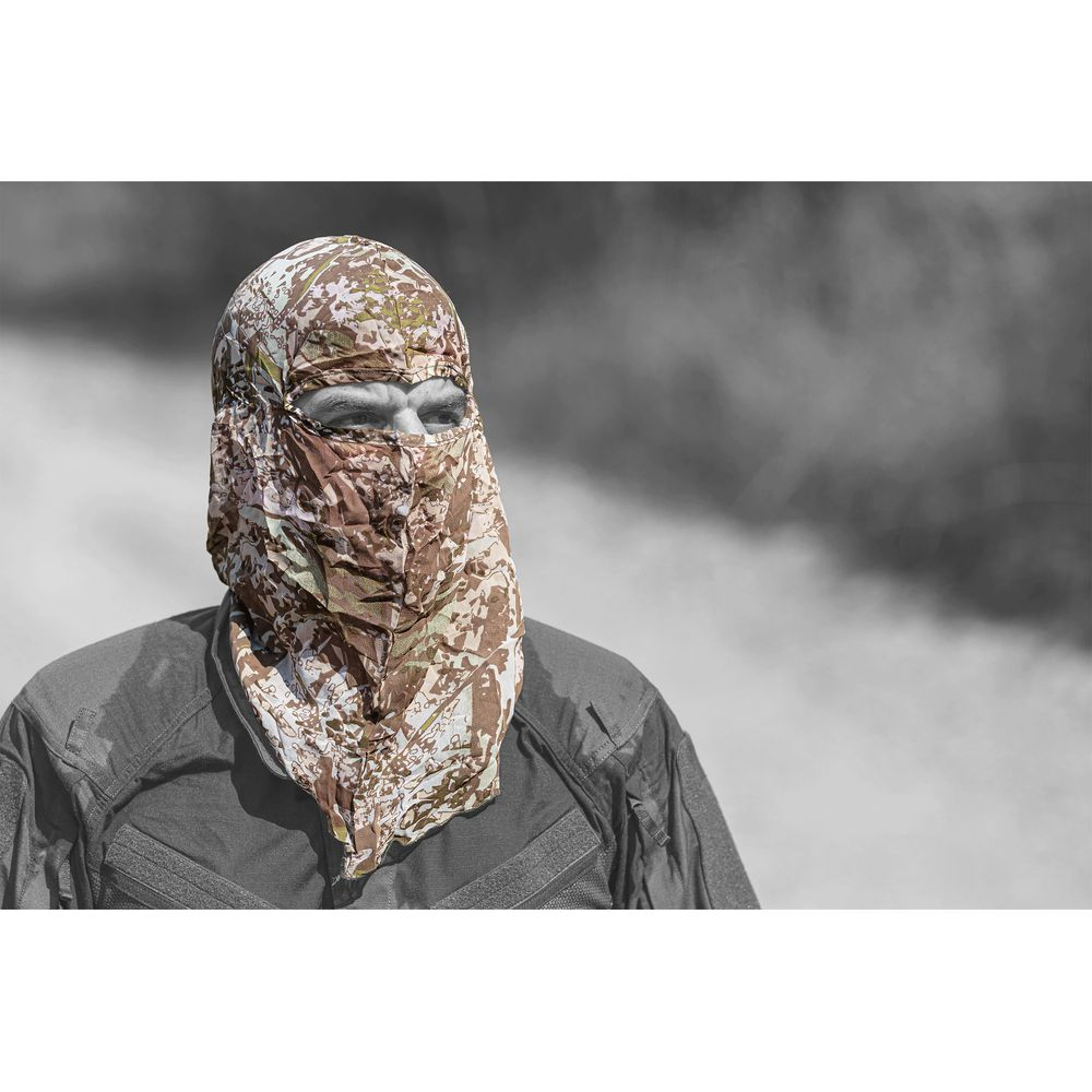 Un uomo indossa una maschera mimetica e una camicia scura su sfondo sfocato.