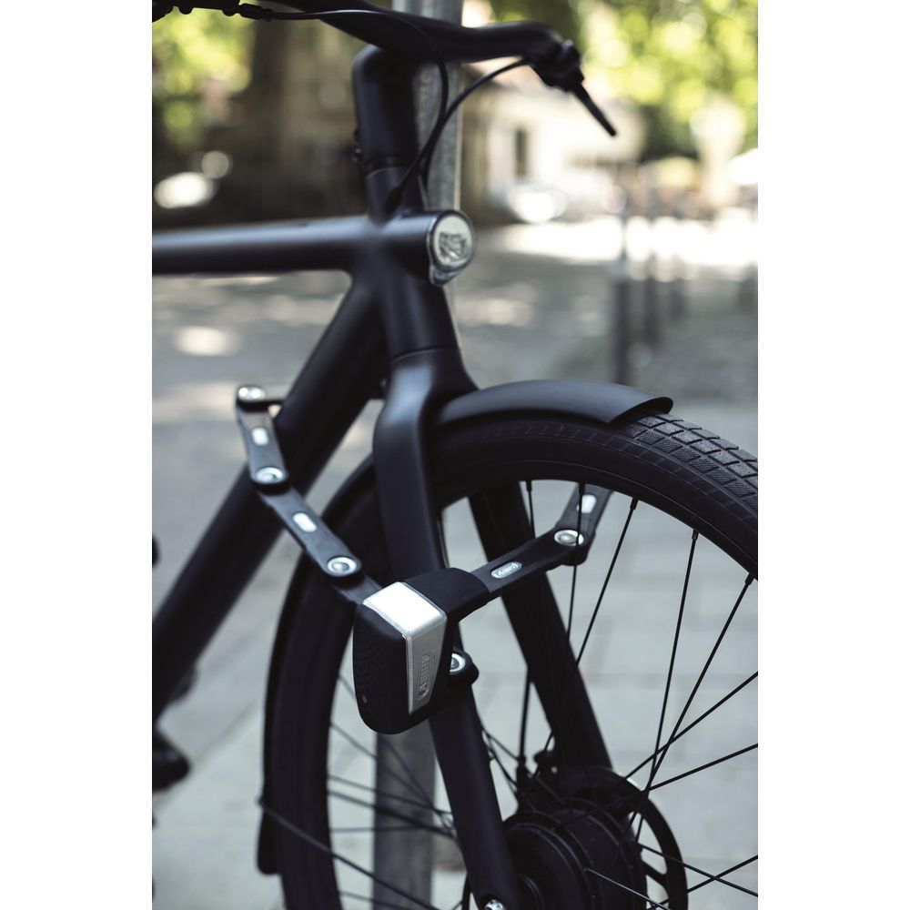 Schwarzes Fahrrad mit Faltschloss am Vorderrad, an einem Pfosten angeschlossen.