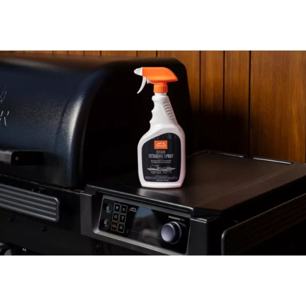 Ein weißer Sprühreiniger mit orangefarbenem Sprühkopf steht auf einem schwarzen Grill.
