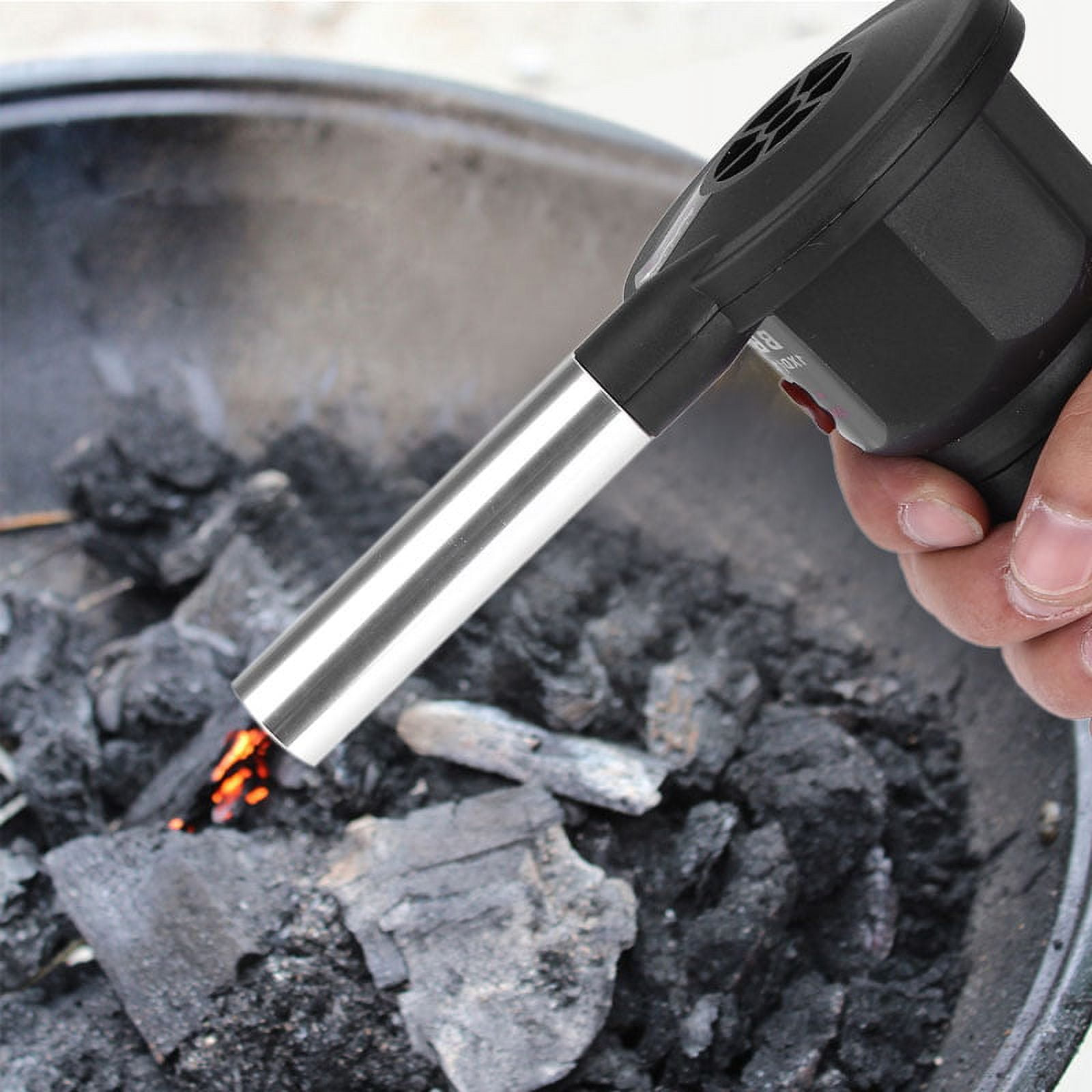Ein schwarzes Gebläse wird über glühende Holzkohle in einem Grill gehalten.