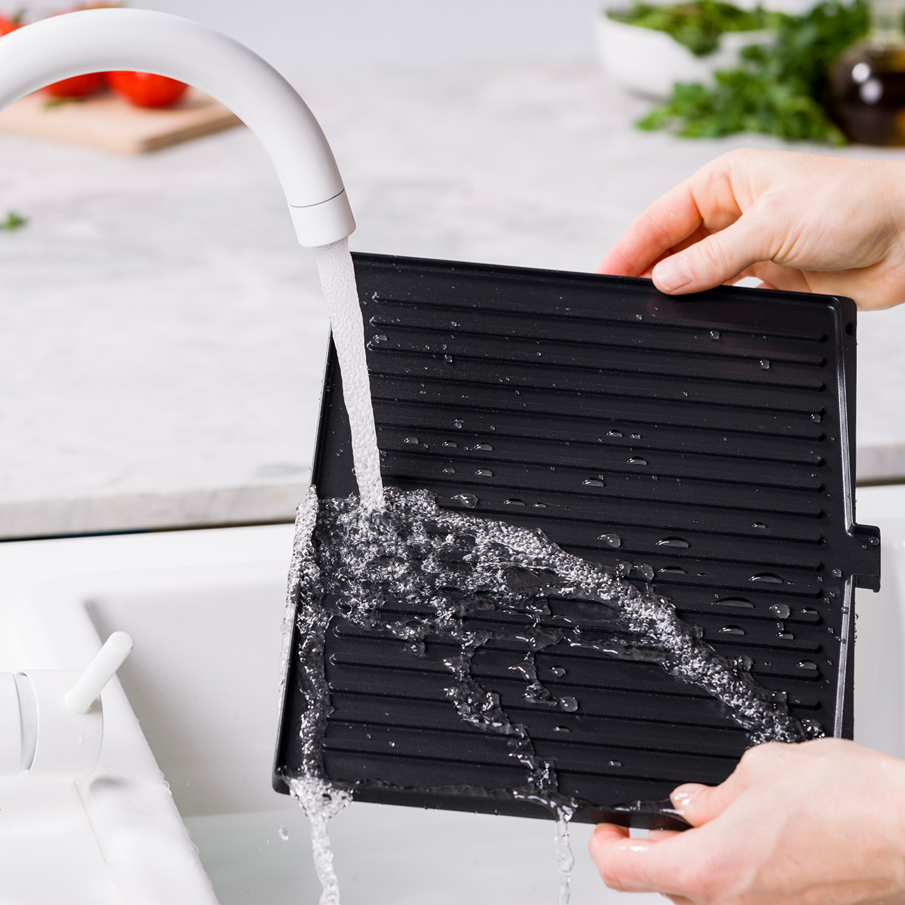 Eine schwarze Grillplatte wird unter fließendem Wasser in einem Spülbecken gespült.