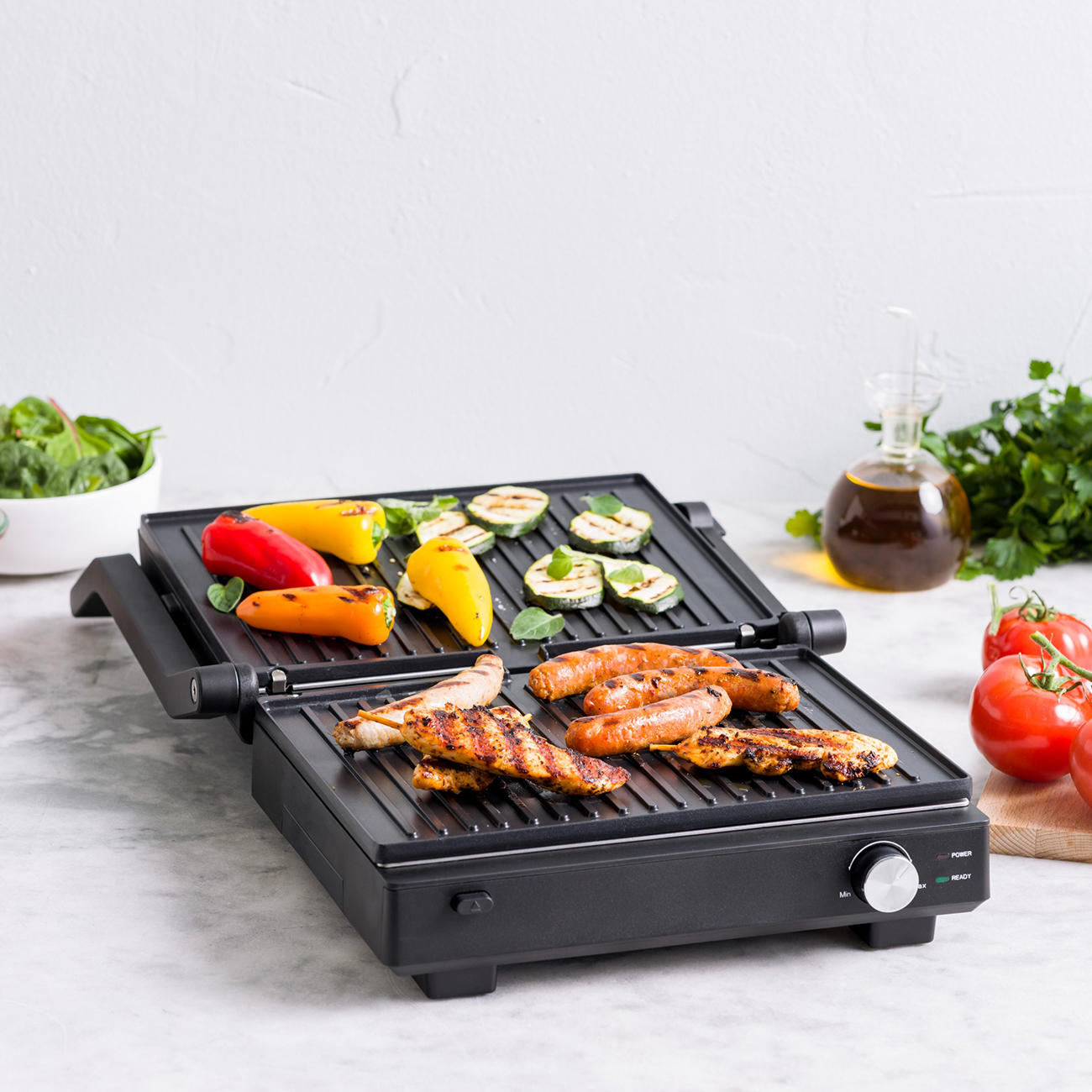 Elektrischer Grill mit Hähnchen, Würstchen, Paprika und Zucchini.