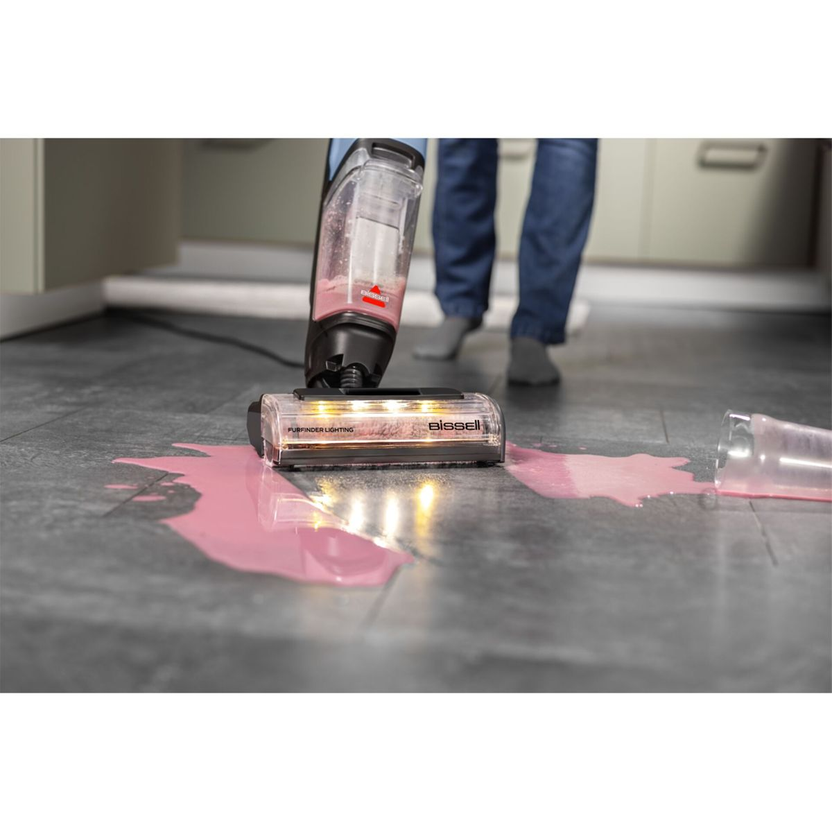 Bodenreiniger mit Licht reinigt verschüttete rosa Flüssigkeit auf dunklem Boden.