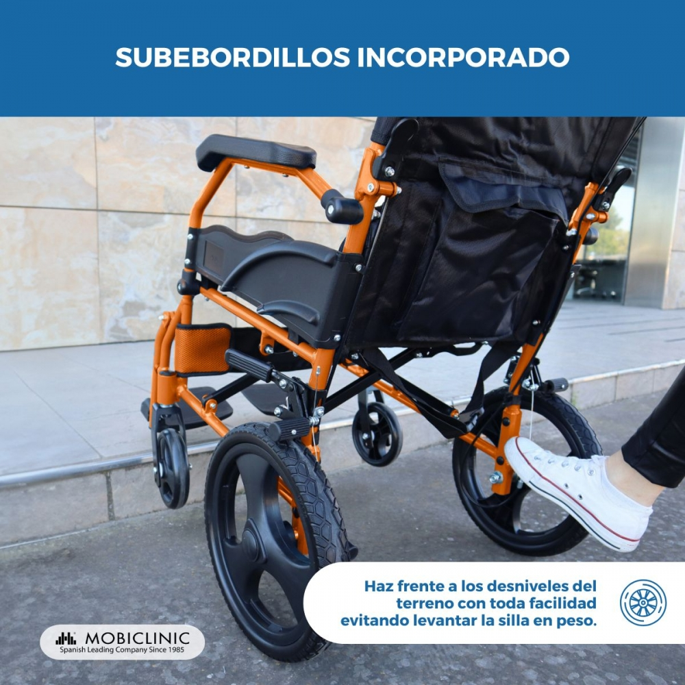 Una silla de ruedas naranja con ruedas negras está al aire libre. Un pie con zapatilla blanca toca la rueda.