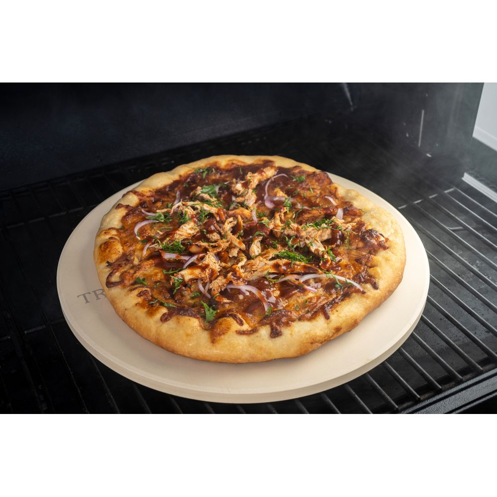Eine BBQ-Hähnchenpizza auf einem Pizzastein im Grill. Mit roten Zwiebeln und Koriander.