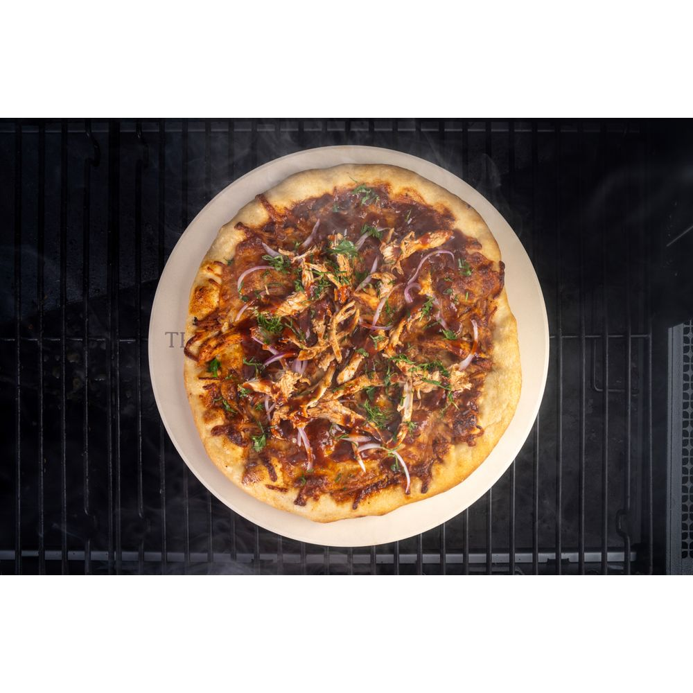 BBQ-Hähnchenpizza mit Zwiebeln und Kräutern auf einem Pizzastein auf einem Grill.