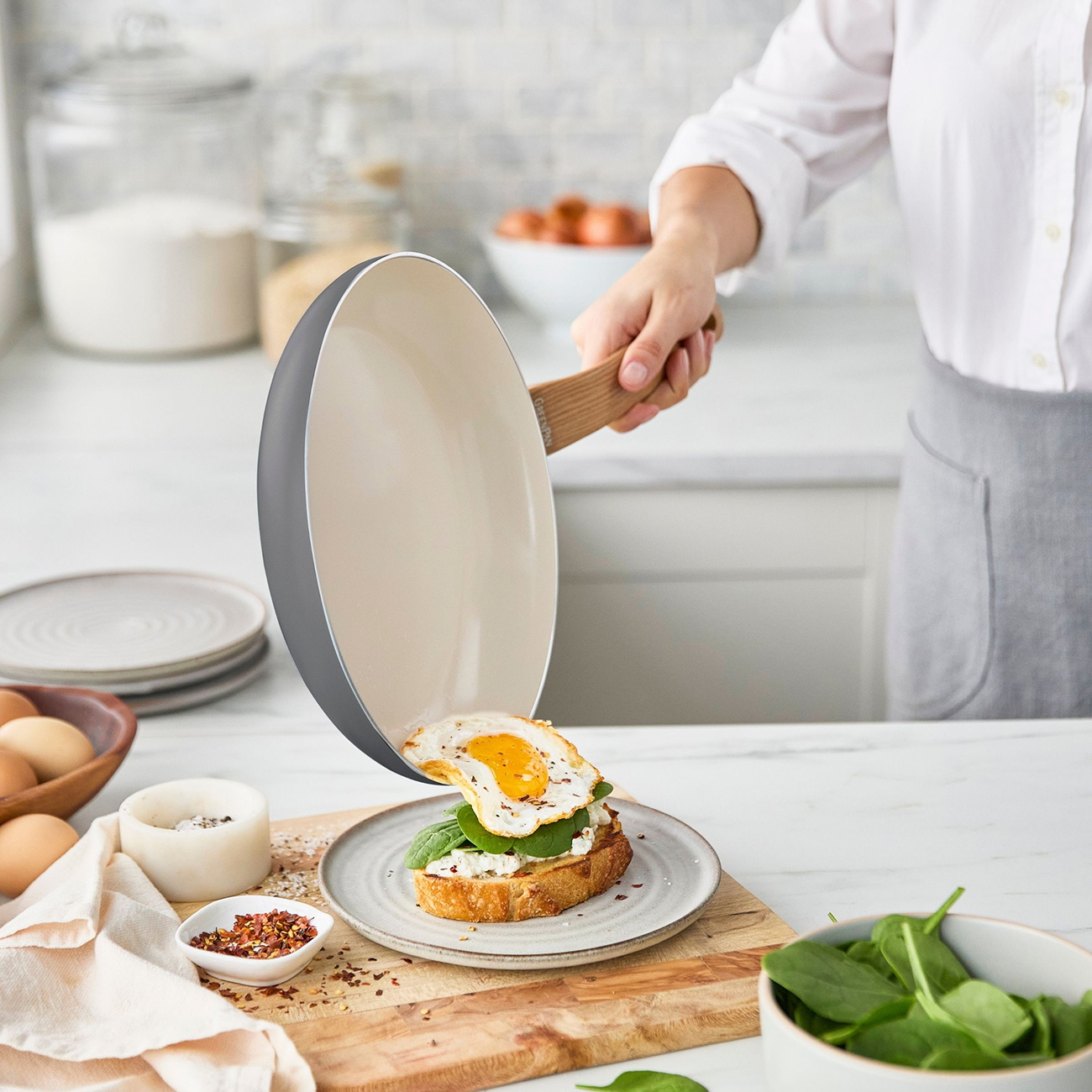 Ein Spiegelei wird auf ein Sandwich mit Spinat und Käse aus einer Pfanne gegeben.