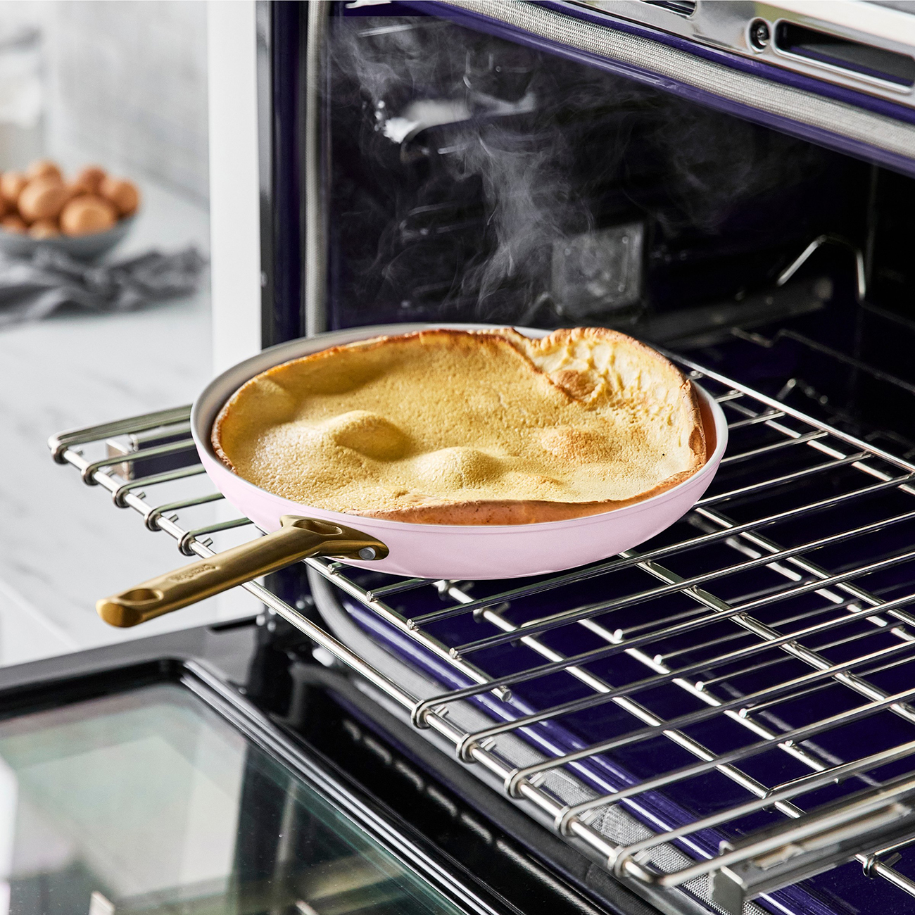 Ein goldbrauner Pfannkuchen gart in einer rosa Pfanne auf einem Ofenrost.