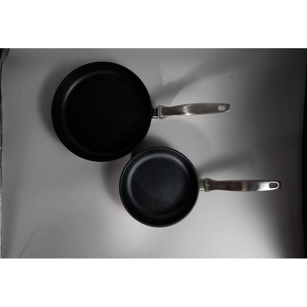 Deux poêles noires avec des poignées argentées sur une surface grise.
