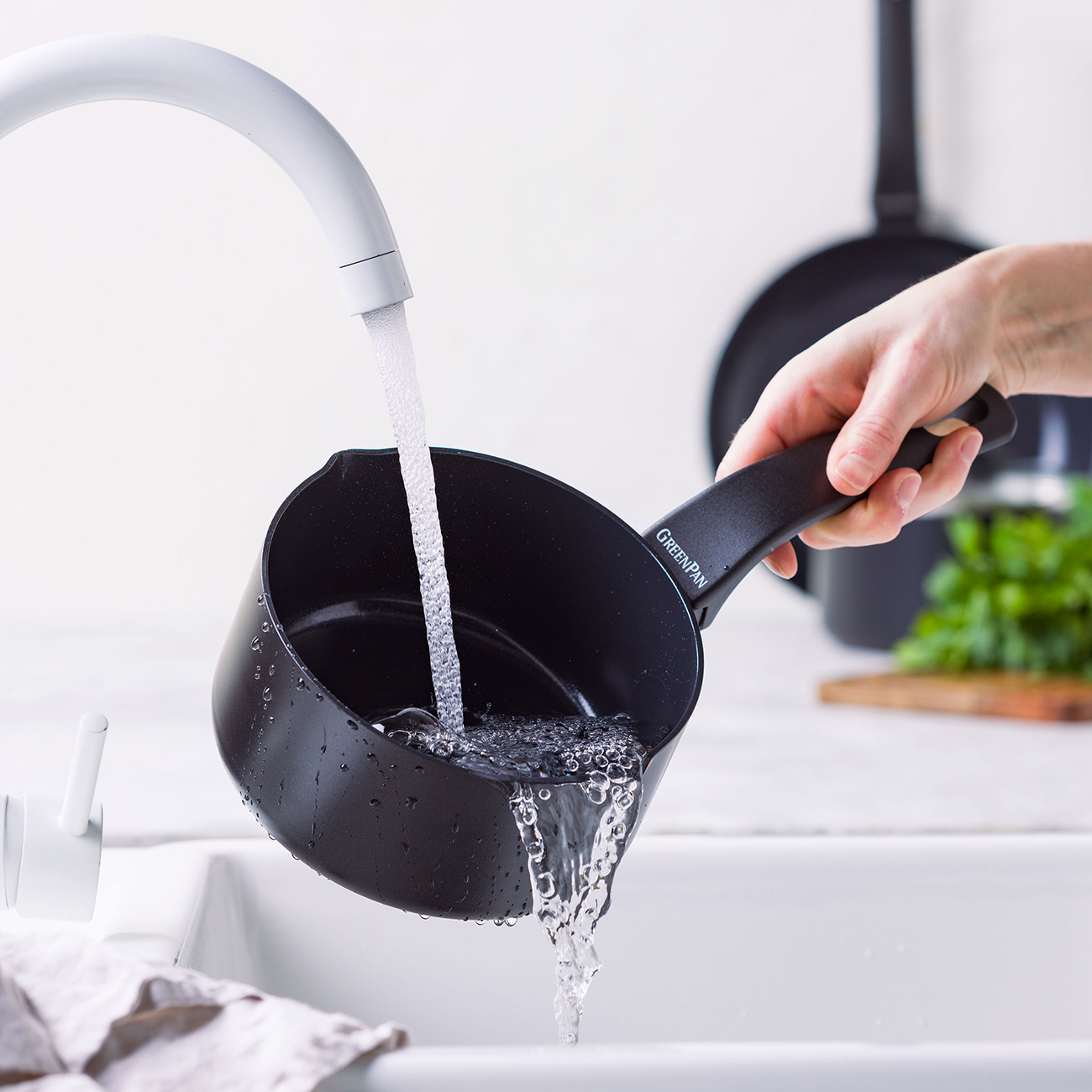 Eine Hand hält eine schwarze Pfanne, während Wasser aus einem Wasserhahn hineinfließt.