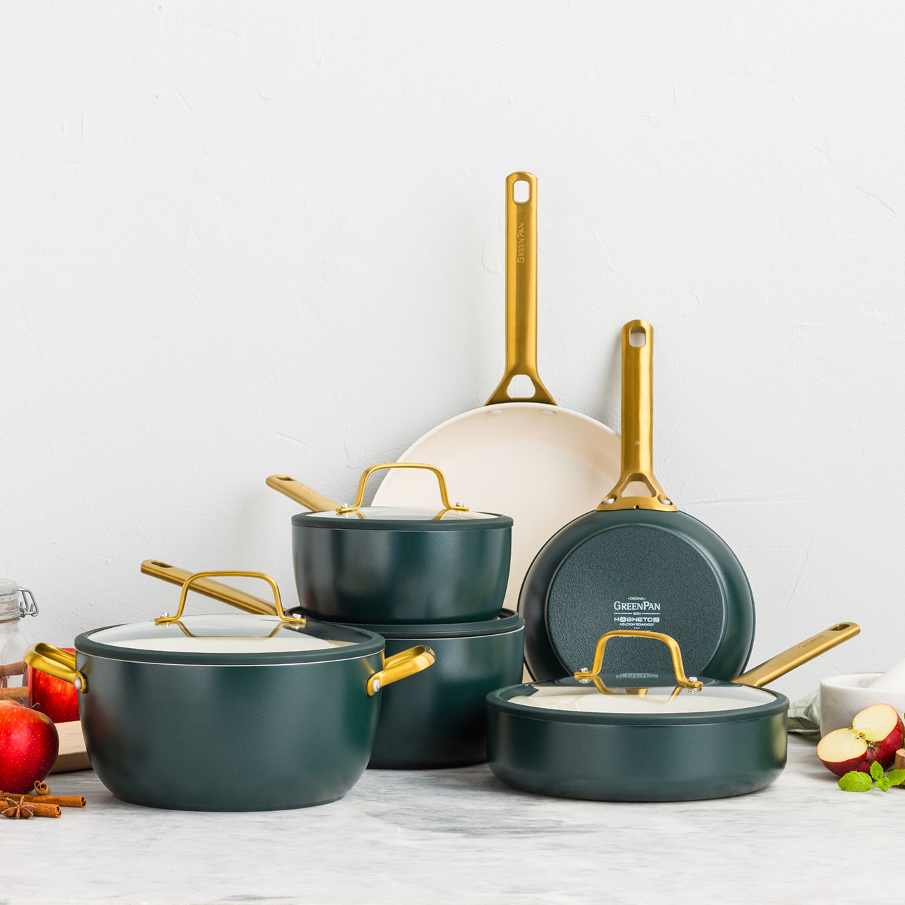 Dunkelgrüne Kochgeschirr-Sets mit goldenen Griffen, Äpfel und Zimt.