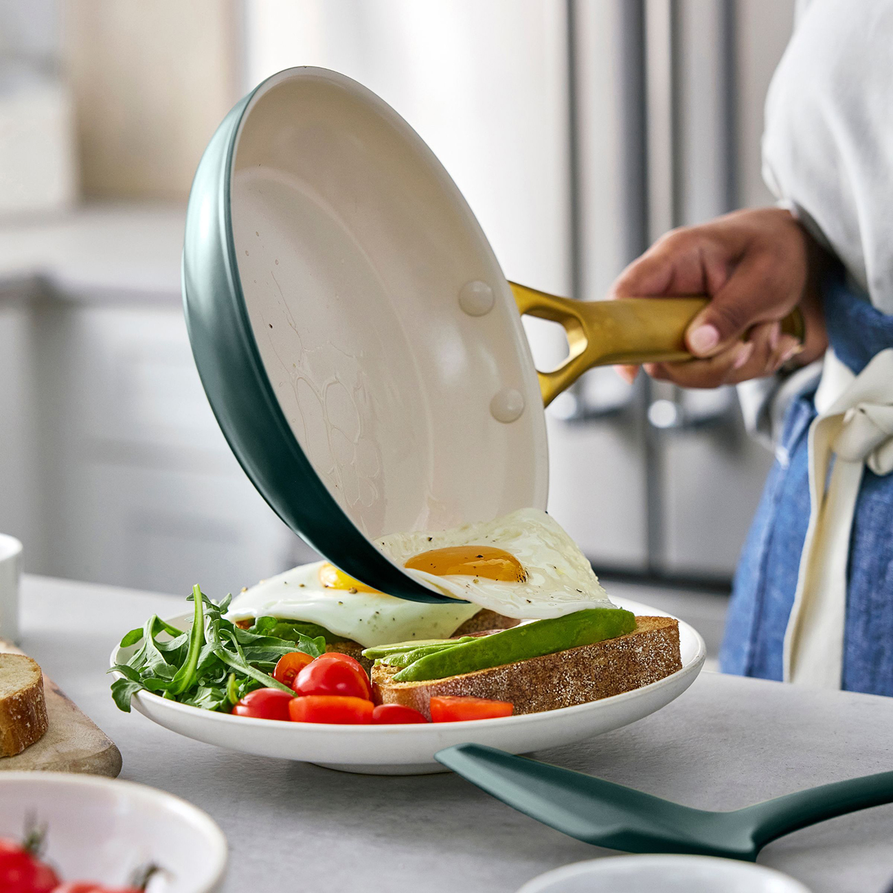 Ein Spiegelei wird aus einer Pfanne auf ein Sandwich mit Avocado und Tomaten gegeben.