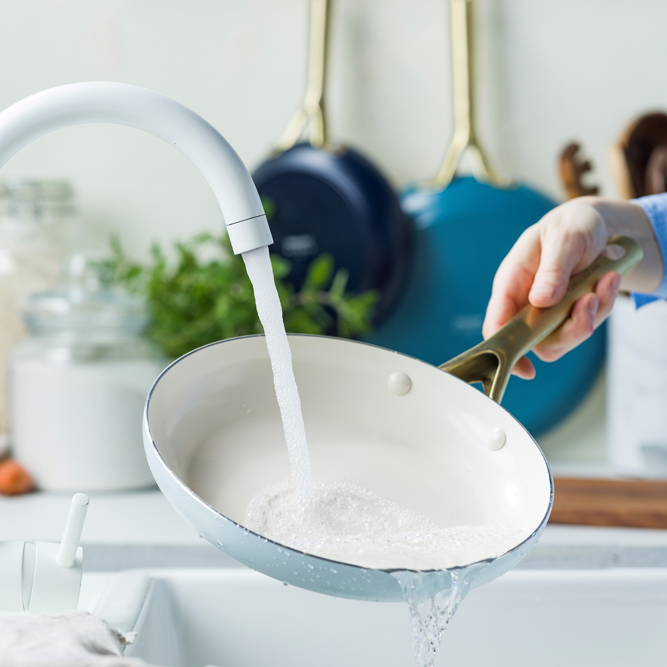 Eine Hand hält eine helle Pfanne unter fließendes Wasser in einer Spüle.