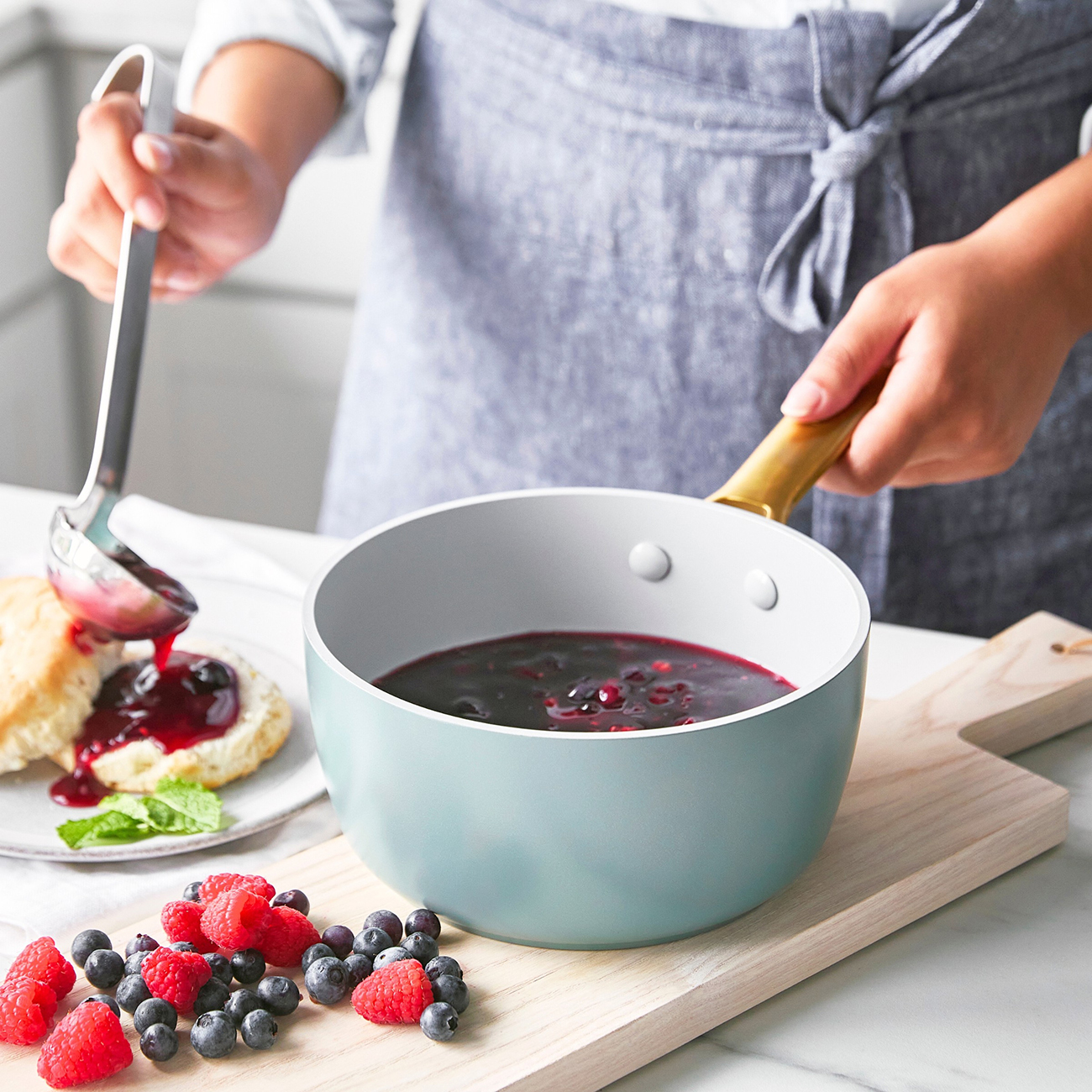 Ein Koch schöpft Blaubeersauce aus einem Topf auf Kekse, daneben Beeren.