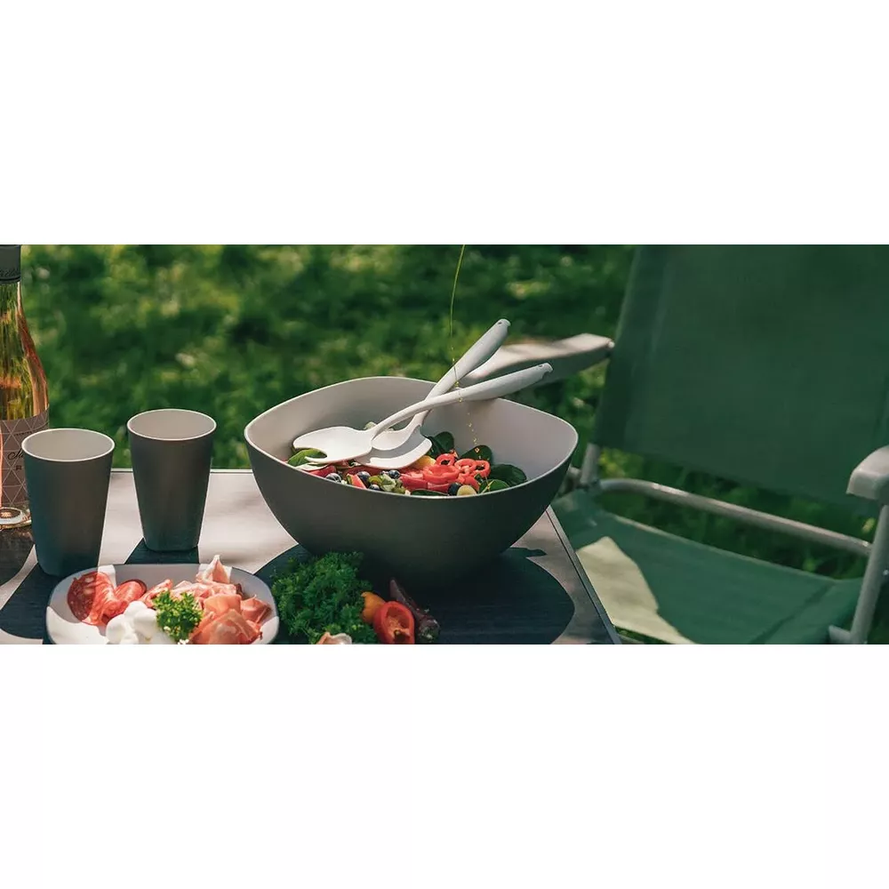 Ein Gartentisch mit Salat, Beilagen und Getränken im Freien.