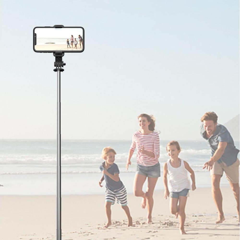 Ein Selfie-Stick mit einem Handy auf einem Strand mit einer Familie, die im Hintergrund rennt.