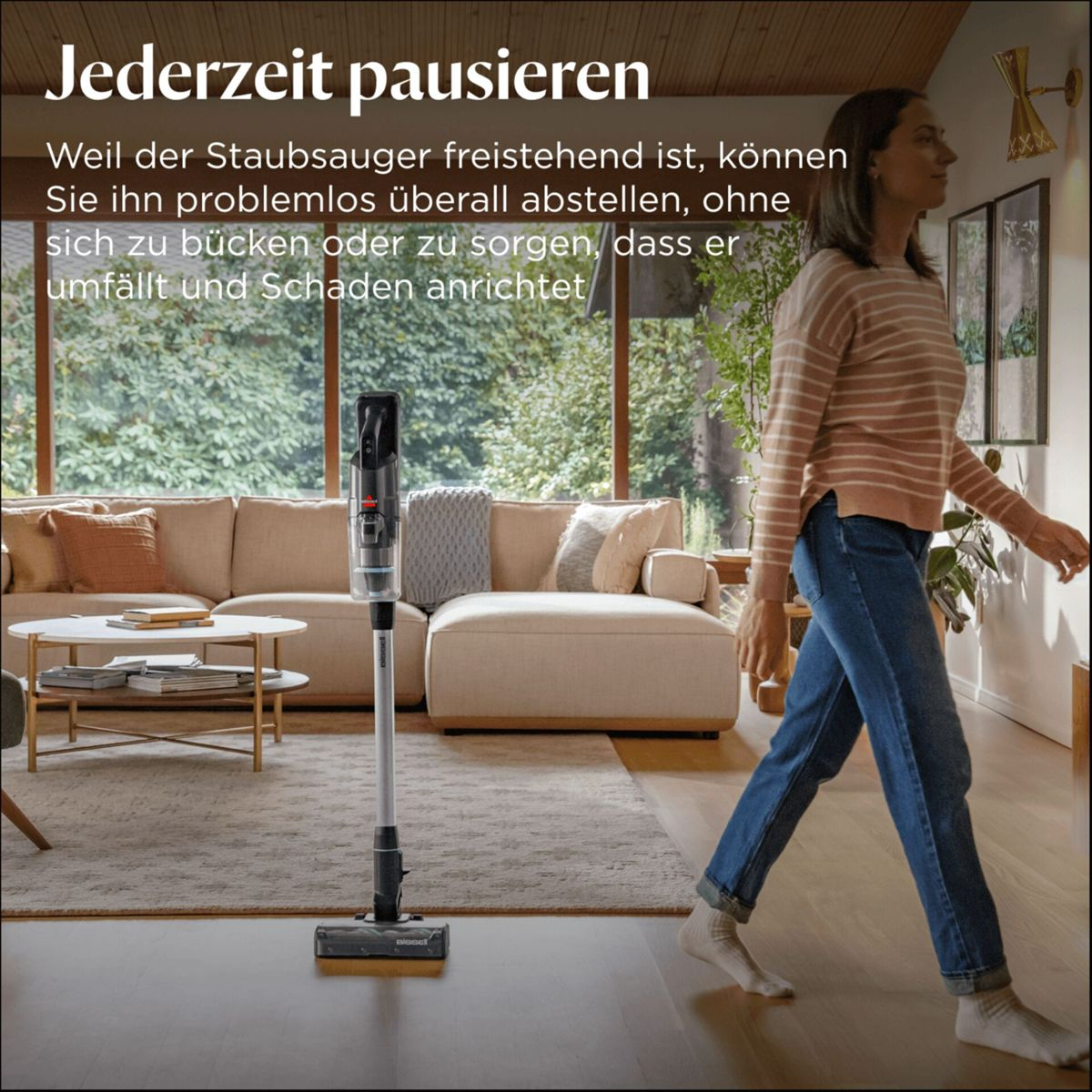 Ein freistehender Staubsauger steht im Wohnzimmer neben einem Sofa.