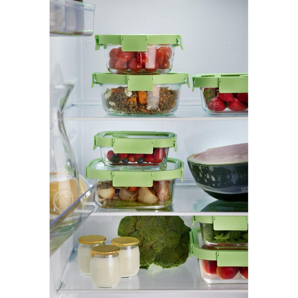 Un frigorifero con contenitori di vetro impilati pieni di cibo e frutta.