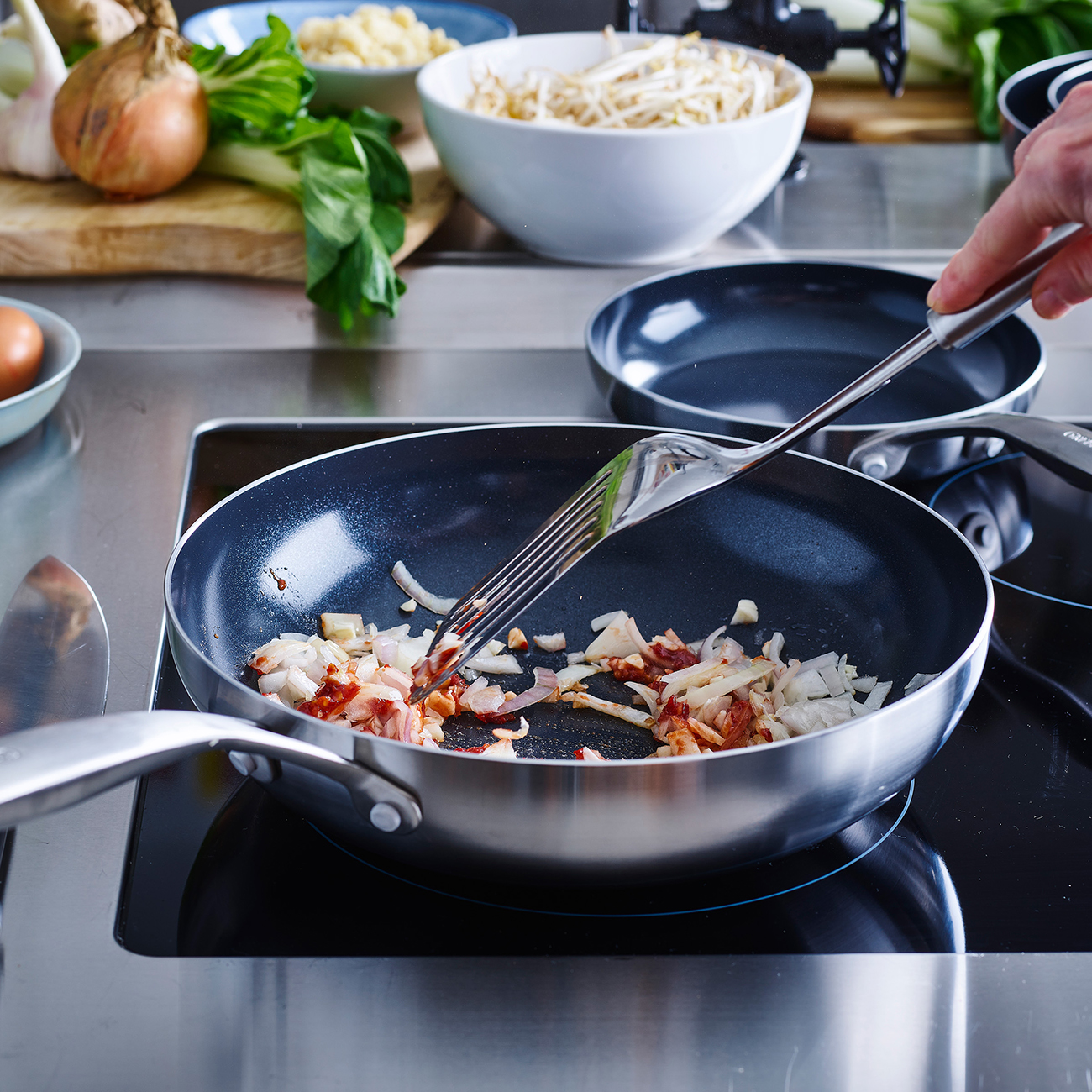 Zwiebeln und Speck werden in einer Pfanne gebraten. Im Hintergrund sind Ingwer, Knoblauch, Eier und Sojasprossen.