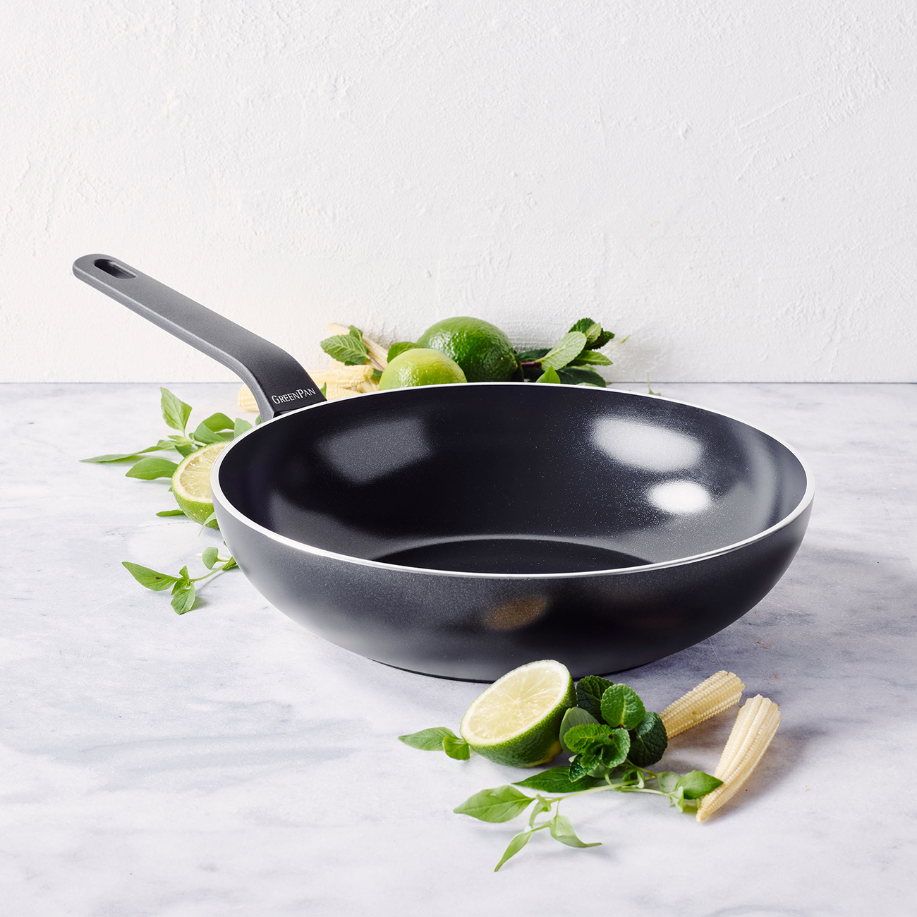 Ein schwarzer Wok mit Zitronenscheiben, Minze und Babymais auf Marmor.