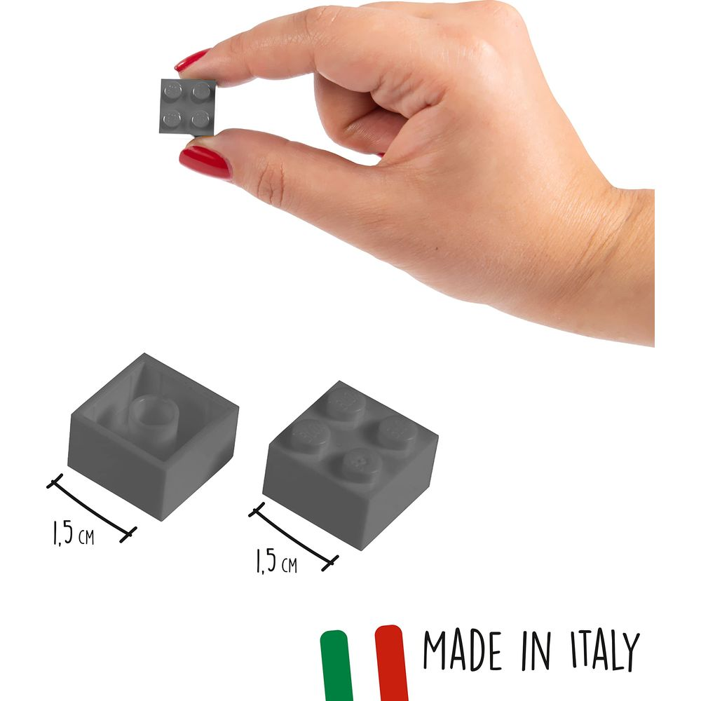Una mano tiene un piccolo mattoncino grigio. Accanto ci sono altri due mattoncini.