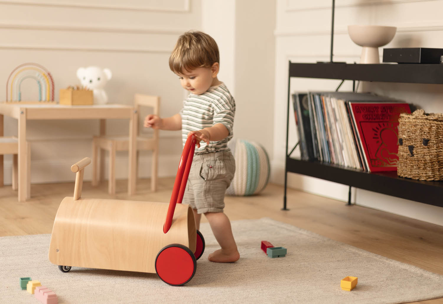 Ein Kleinkind schiebt einen Holzroller mit roten Griffen und Rädern.