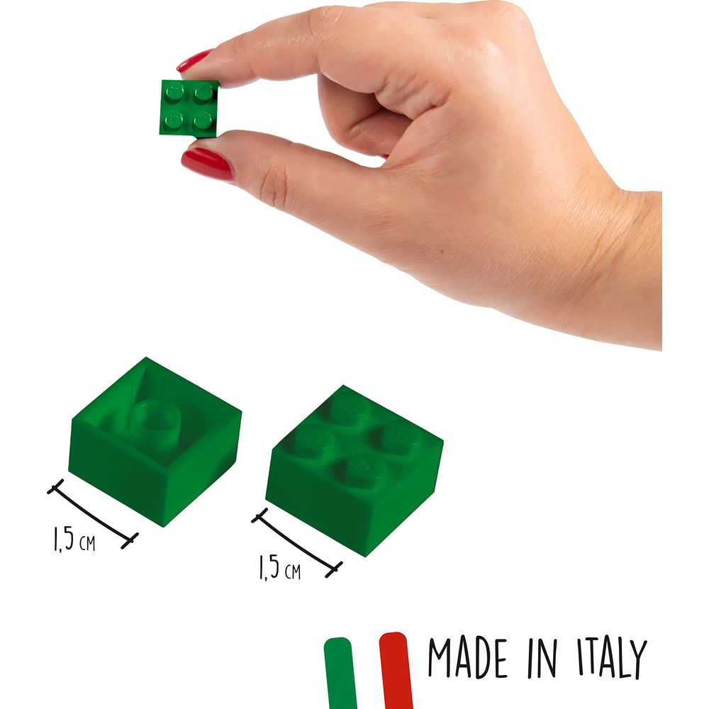 Una mano tiene un piccolo mattoncino Lego verde. Accanto ci sono altri due mattoncini.