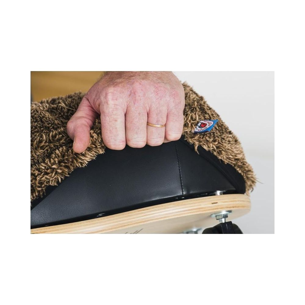 Eine Hand greift nach einem braunen, flauschigen Bezug auf einem schwarzen Sitz mit Holzunterlage.