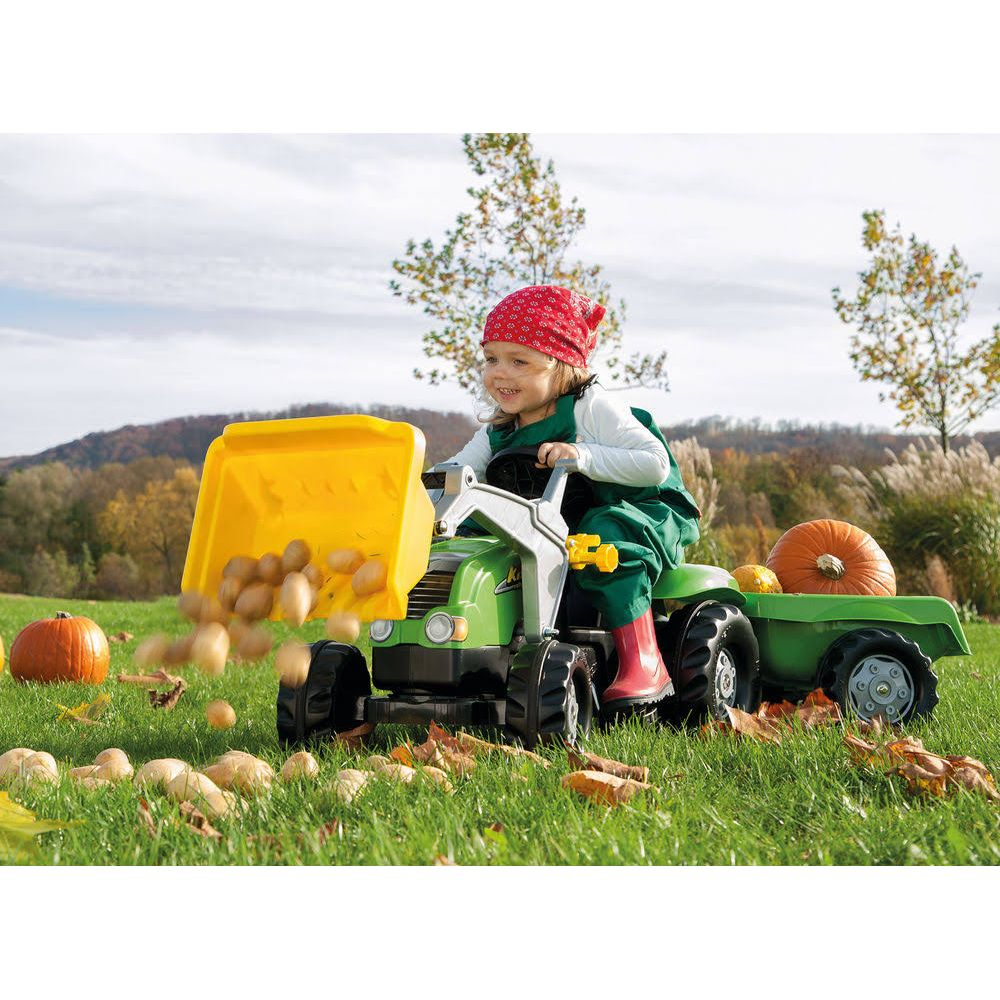 Kind in grüner Latzhose fährt grünen Spielzeugtraktor mit gelber Schaufel voller Kartoffeln.