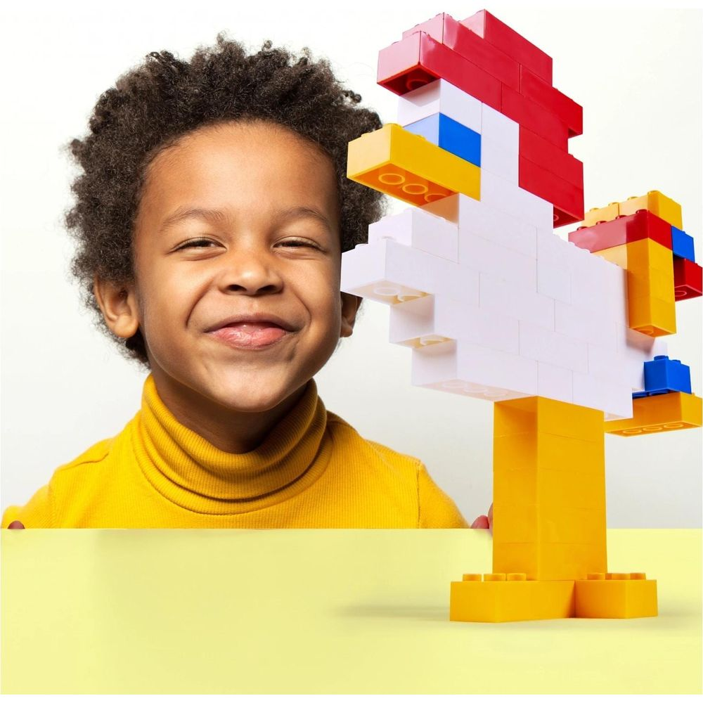 Un garçon en pull à col roulé jaune sourit à côté d'un poulet en blocs de construction colorés.