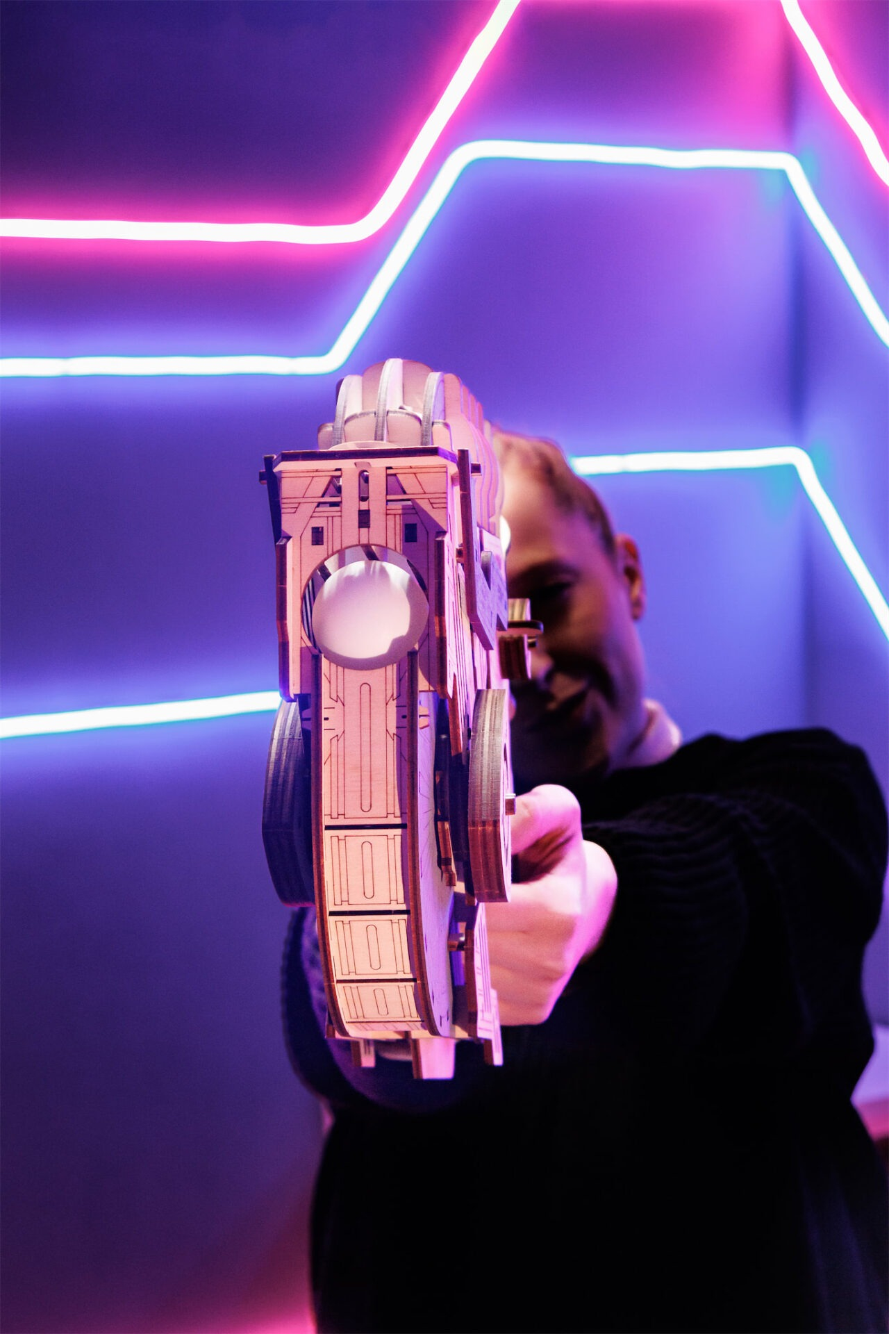 Mann zielt mit Holzspielzeuggewehr vor Neonlichtern.