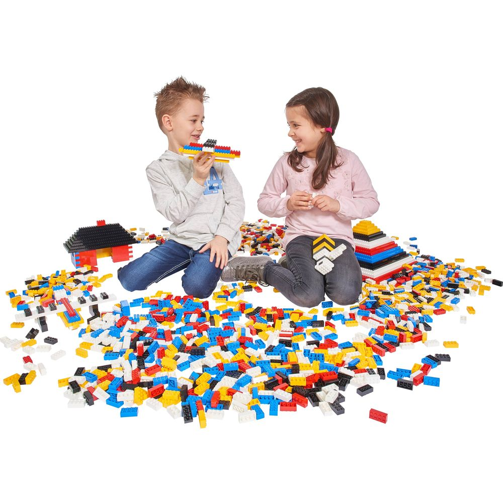 Zwei Kinder sitzen inmitten vieler bunter Bausteine. Eines hält ein Flugzeug.