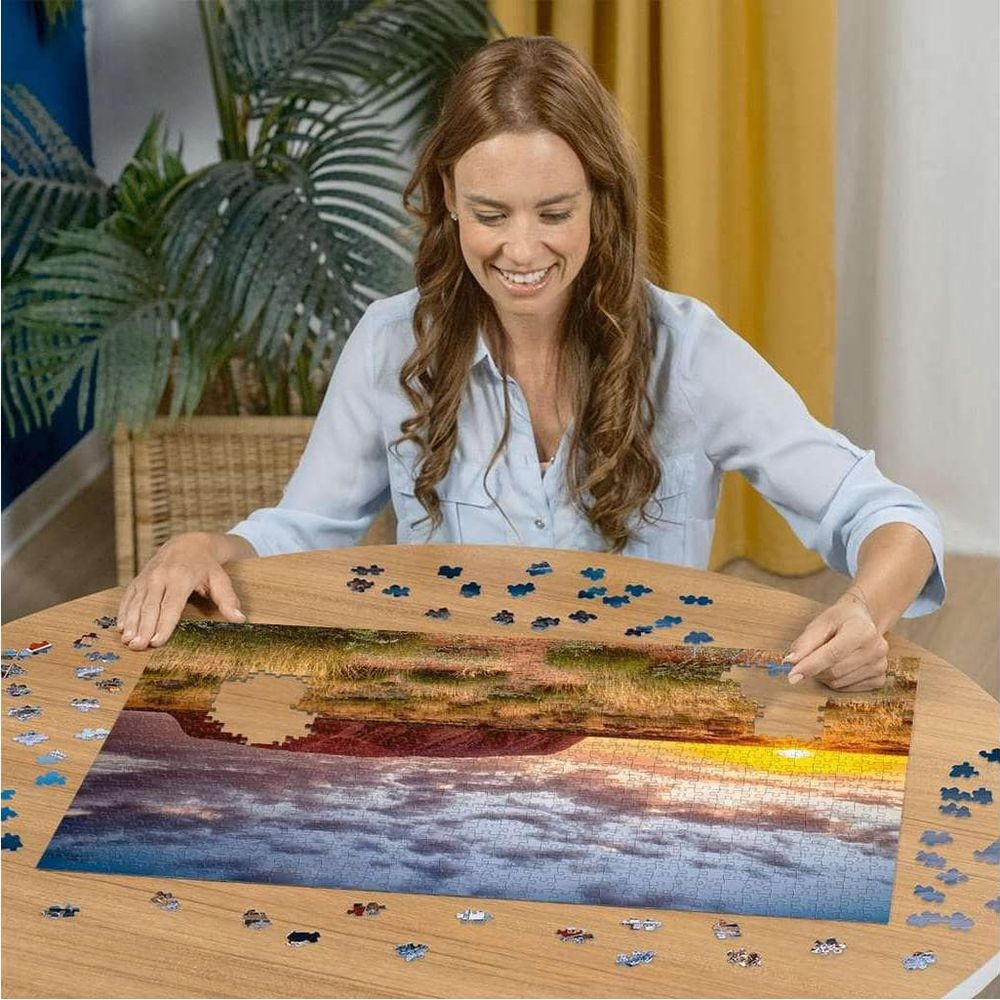 Frau löst ein Puzzle mit Landschaftsbild bei Sonnenuntergang.