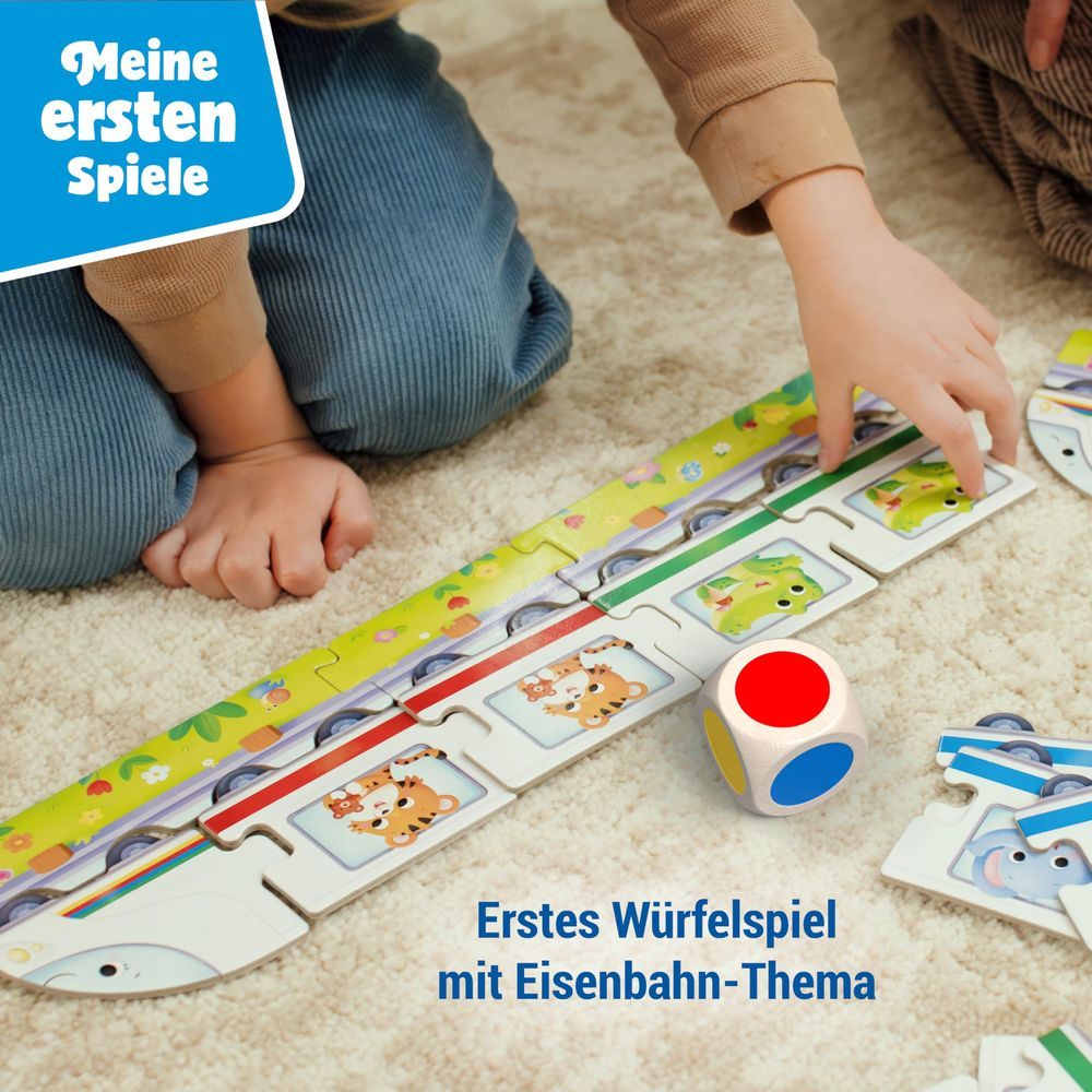 Kinder spielen mit einem Eisenbahn-Puzzle und Würfel auf einem Teppich.
