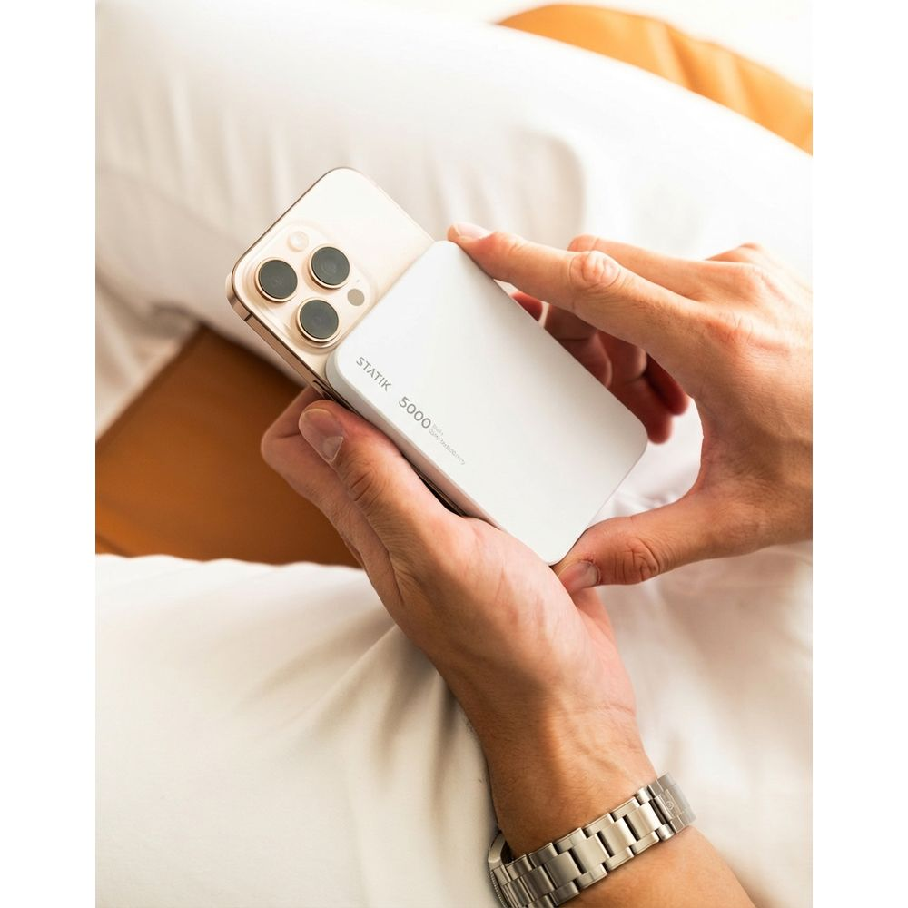Eine Person hält ein weißes Ladegerät und ein goldenes Smartphone.
