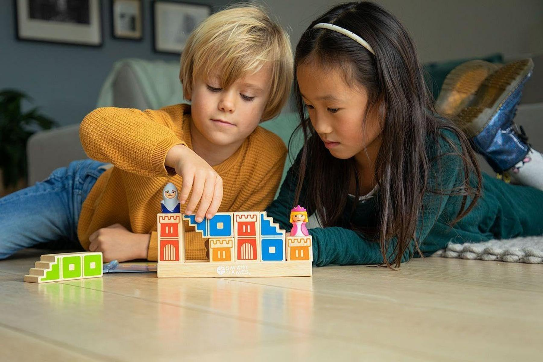Zwei Kinder spielen mit Holzschlössern und Figuren auf dem Boden.