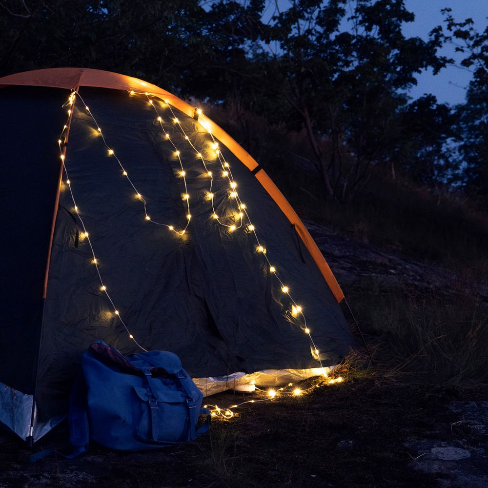 Una tenda con catena luminosa di notte, zaino blu davanti.