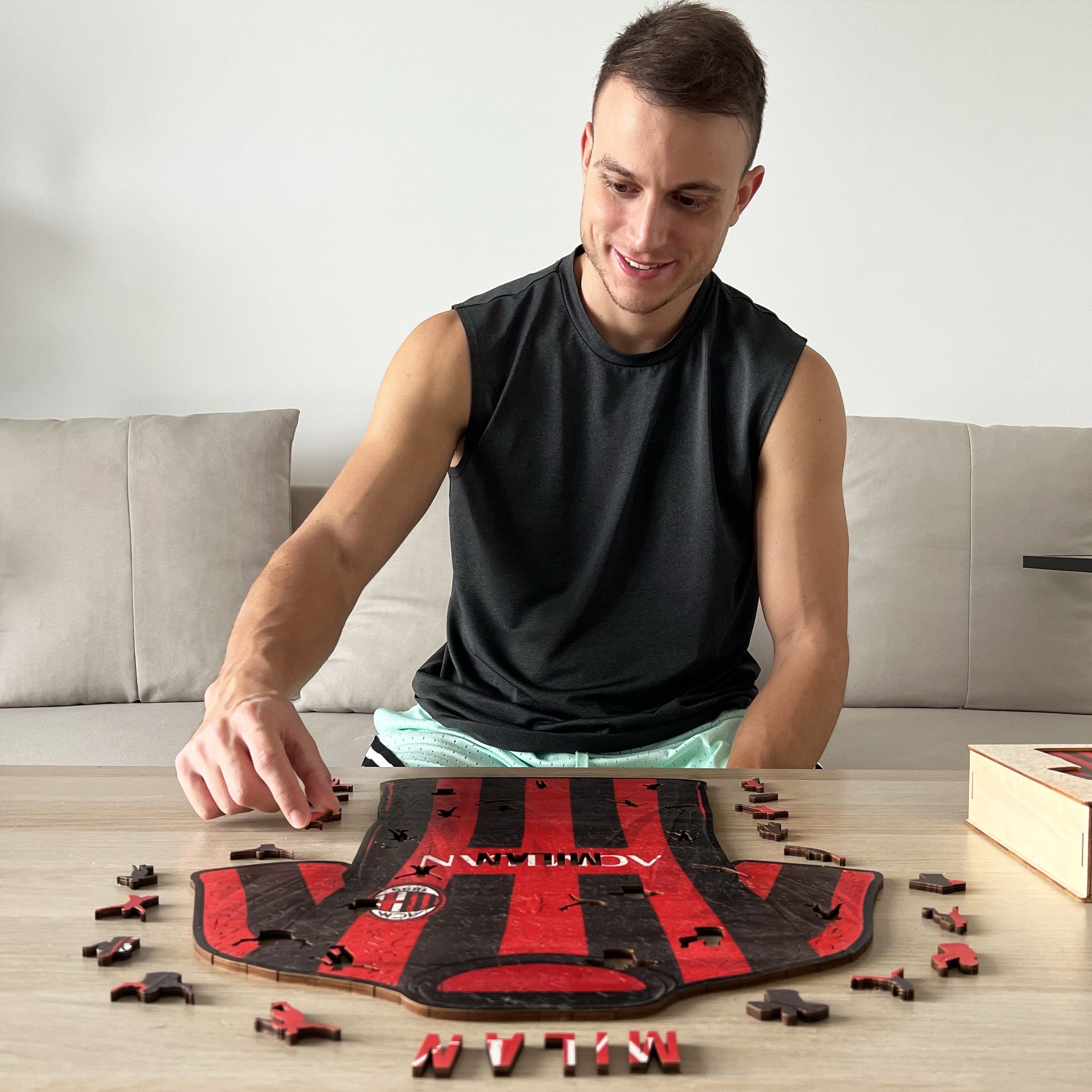 Ein Mann baut ein Puzzle in Form eines Fußballtrikots. Er sitzt an einem Tisch.