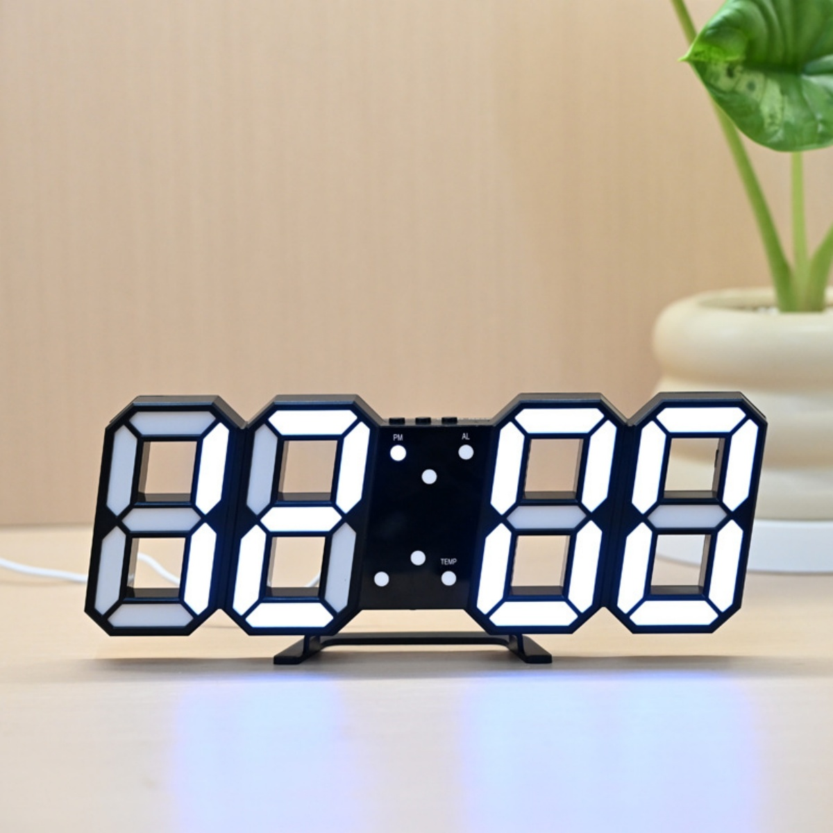 Eine schwarze Digitaluhr mit weißen LED-Zahlen zeigt 08:08 an, im Hintergrund eine Pflanze in einem weißen Topf.