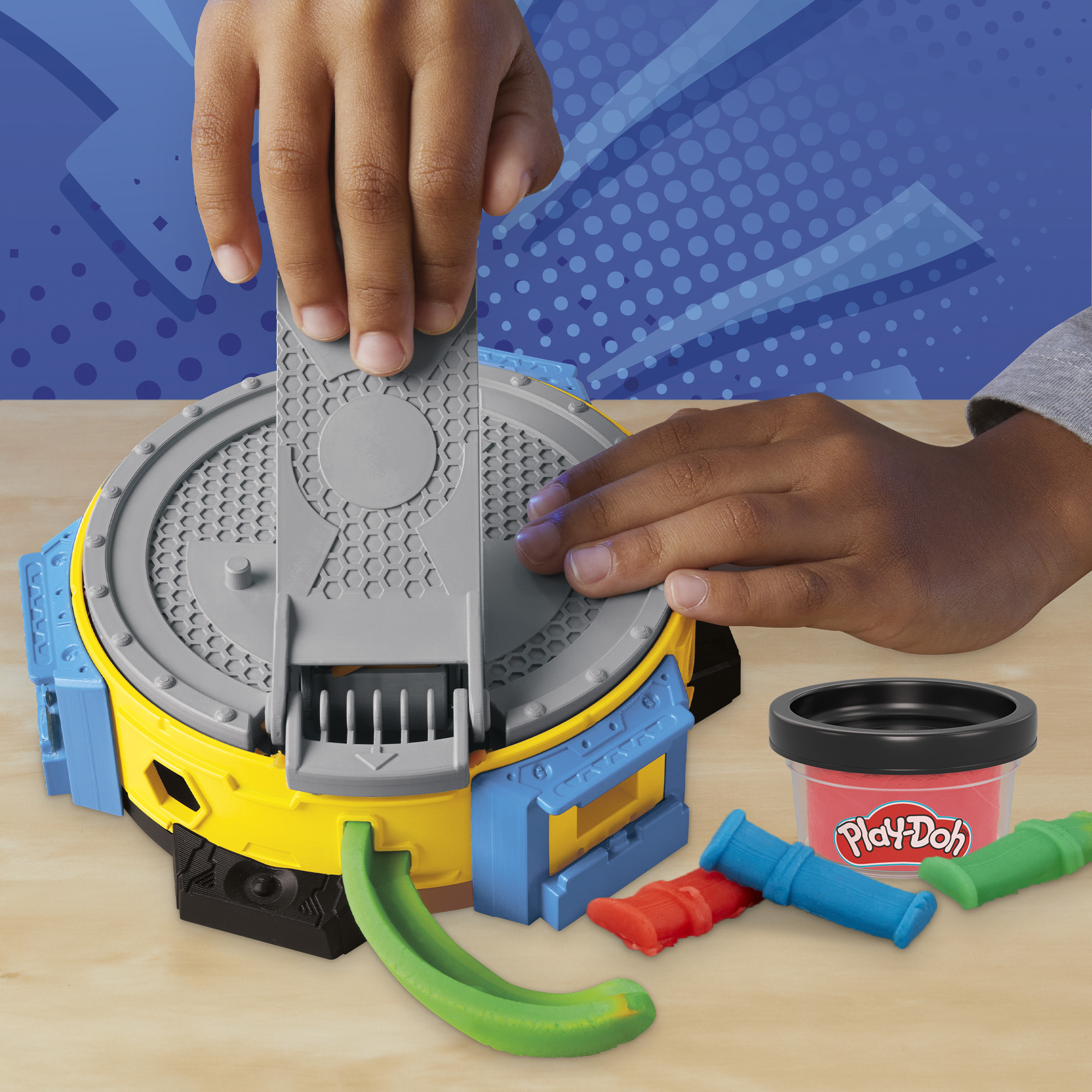Hände bedienen ein gelbes, blaues und graues Play-Doh-Spielzeug mit roten, grünen und blauen Extrusionen.