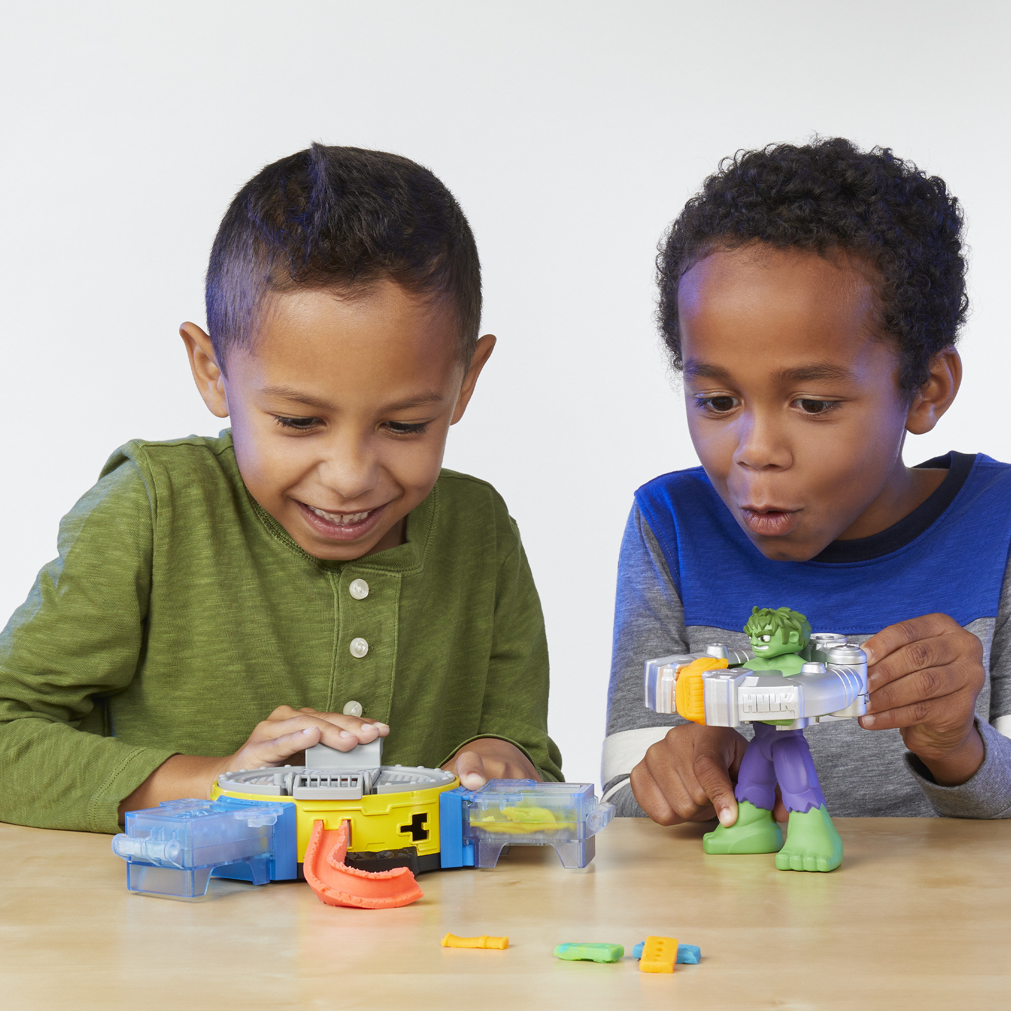 Zwei Jungen spielen mit Spielzeugfiguren und einem Spielset auf einem Holztisch.