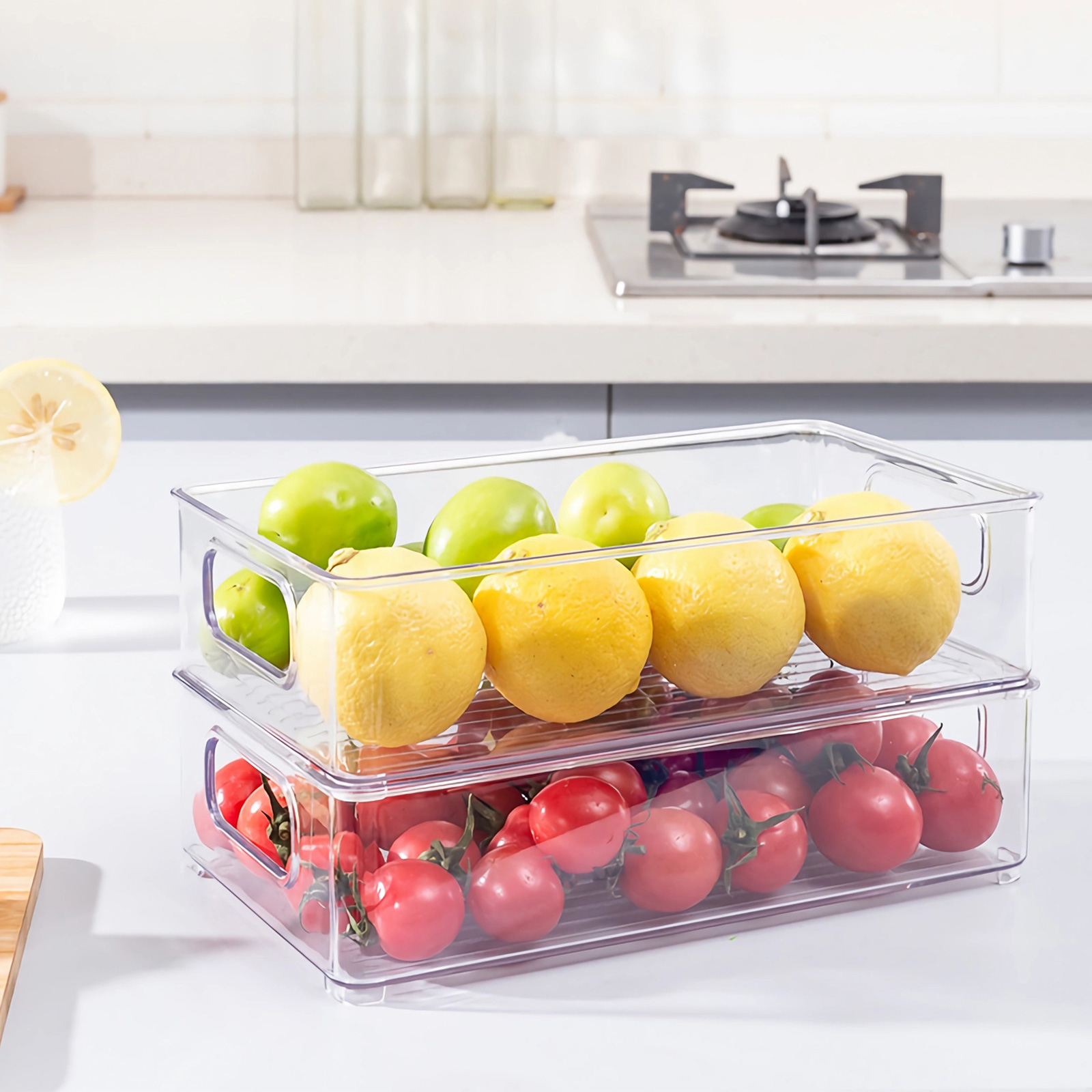 Zwei transparente Behälter mit Obst und Gemüse. Oben Zitronen und grüne Äpfel, unten Tomaten.