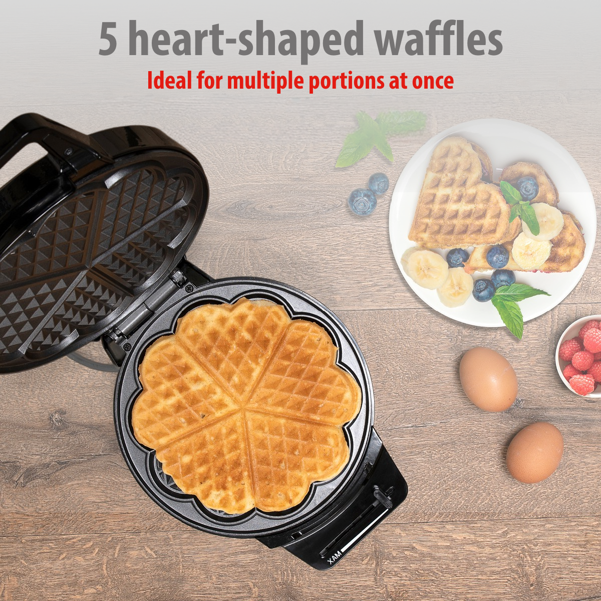 Heart-shaped waffles in an open waffle maker and on a plate with berries.