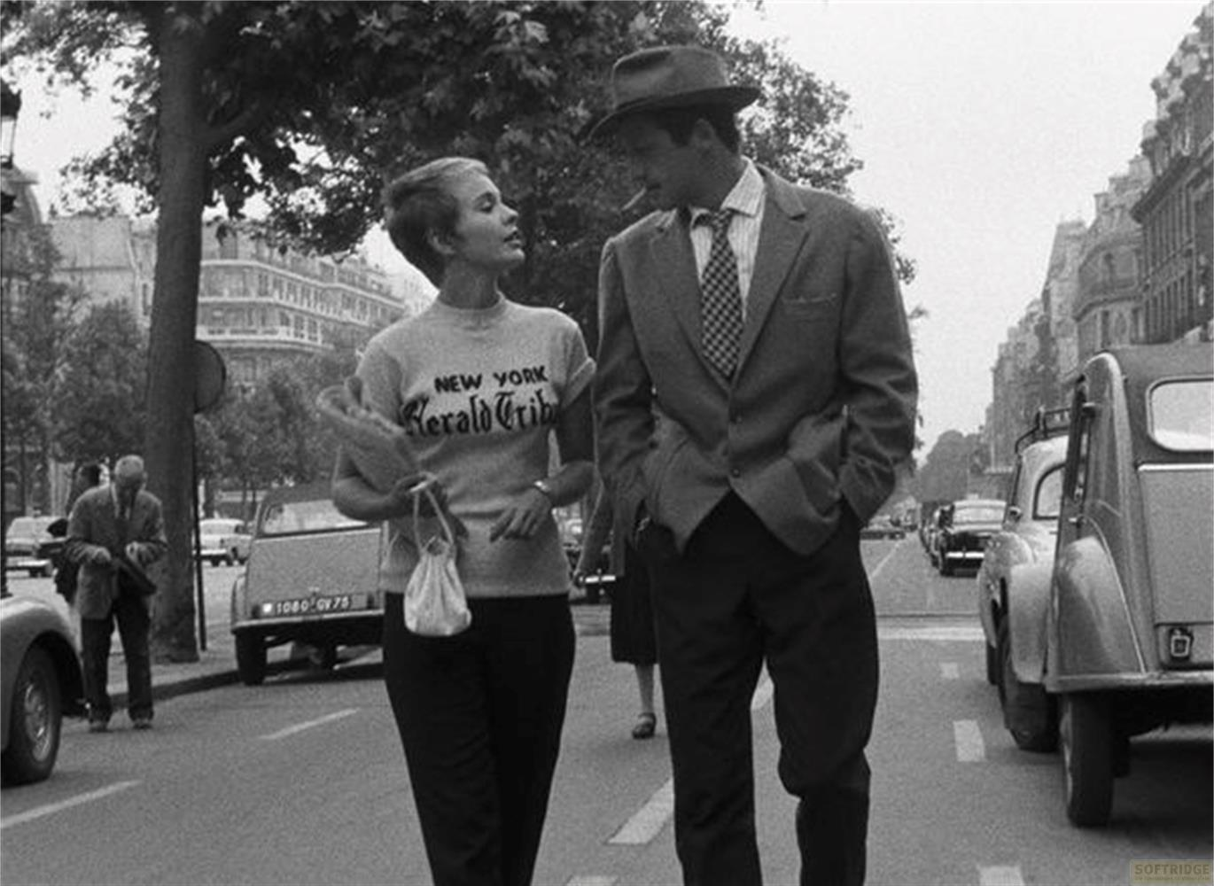 Un uomo con cappello e una donna in t-shirt camminano per una strada di Parigi.