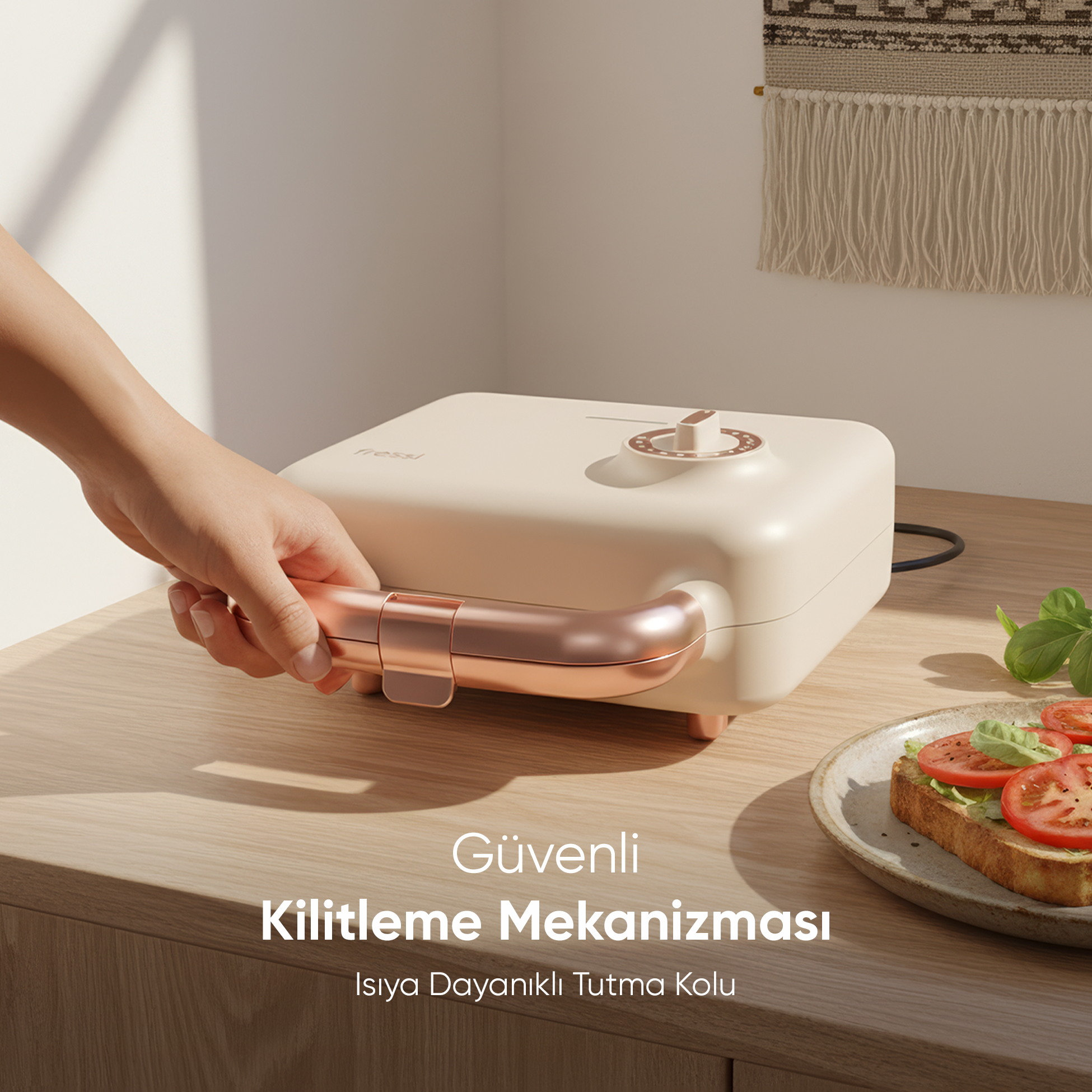 Bir el, rose gold detaylı, krem rengi sandviç makinesinin sapını tutuyor.