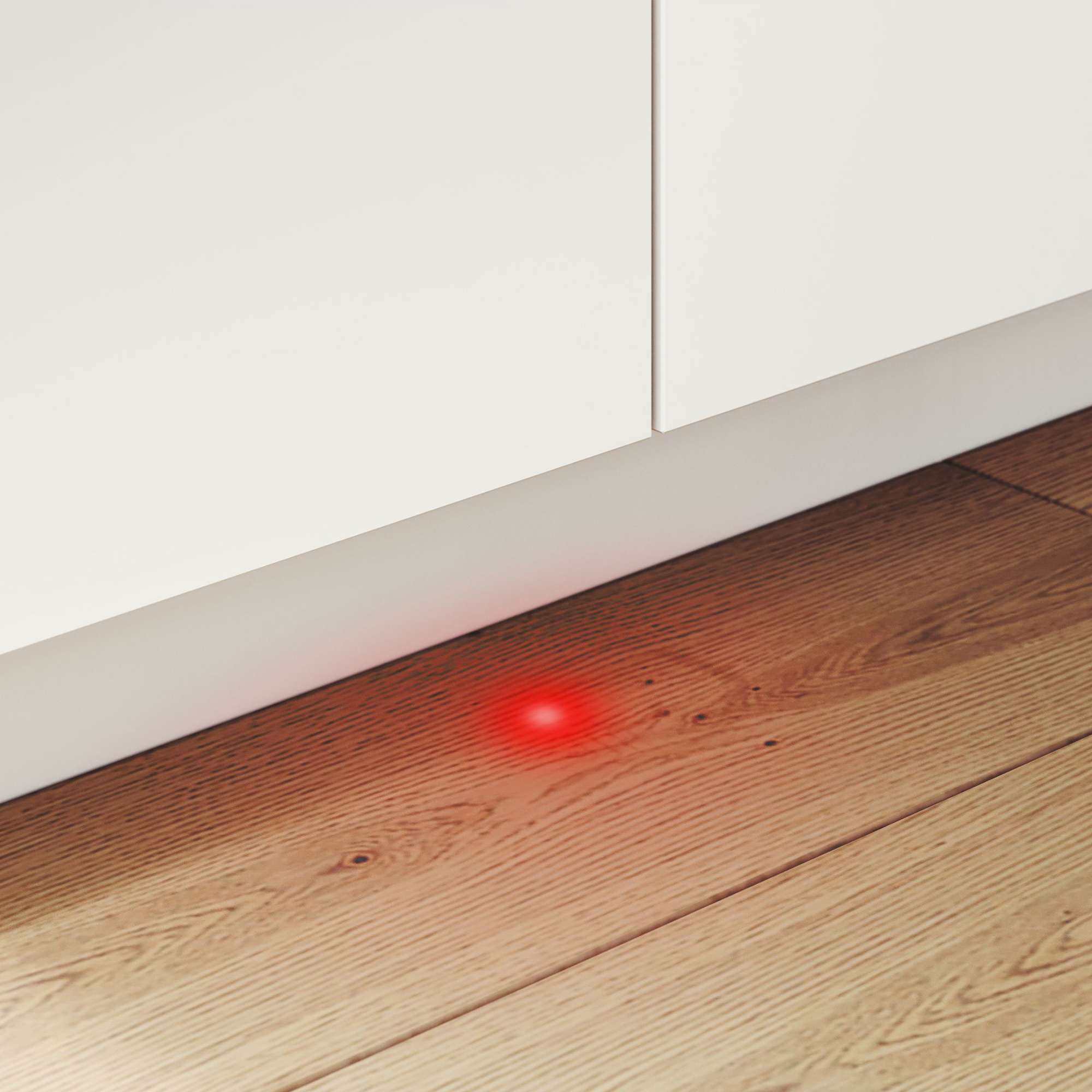 Ein roter Punkt leuchtet auf einem Holzfußboden neben weißen Schränken.
